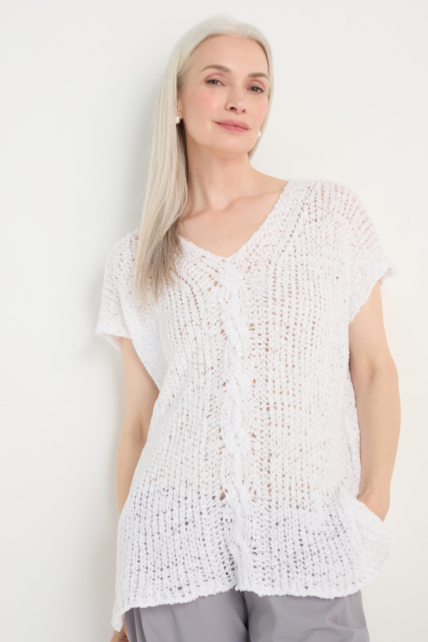 A woman with long gray hair is wearing the V-Neck Cotton Blend Knit in white with light gray pants, standing against a plain white background.