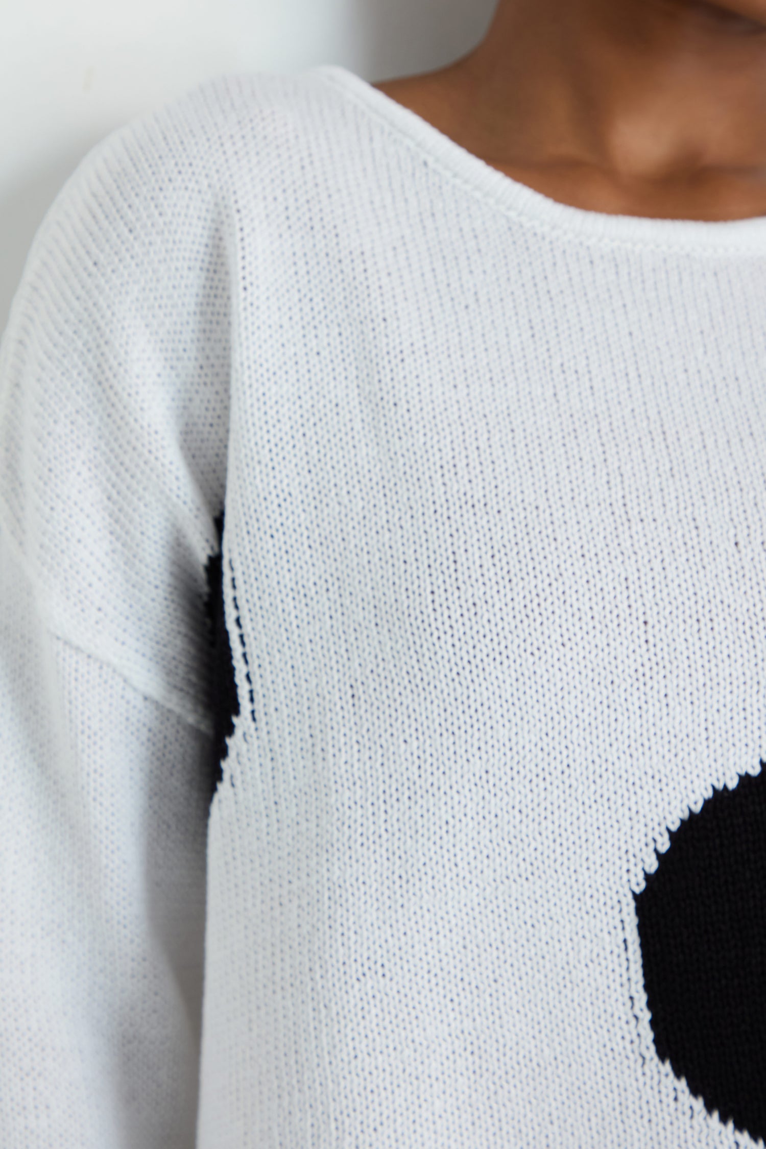 Someone wearing the Spot Cotton Knit, a white organic cotton sweater featuring a black oval elbow patch, shown from shoulder to waist.