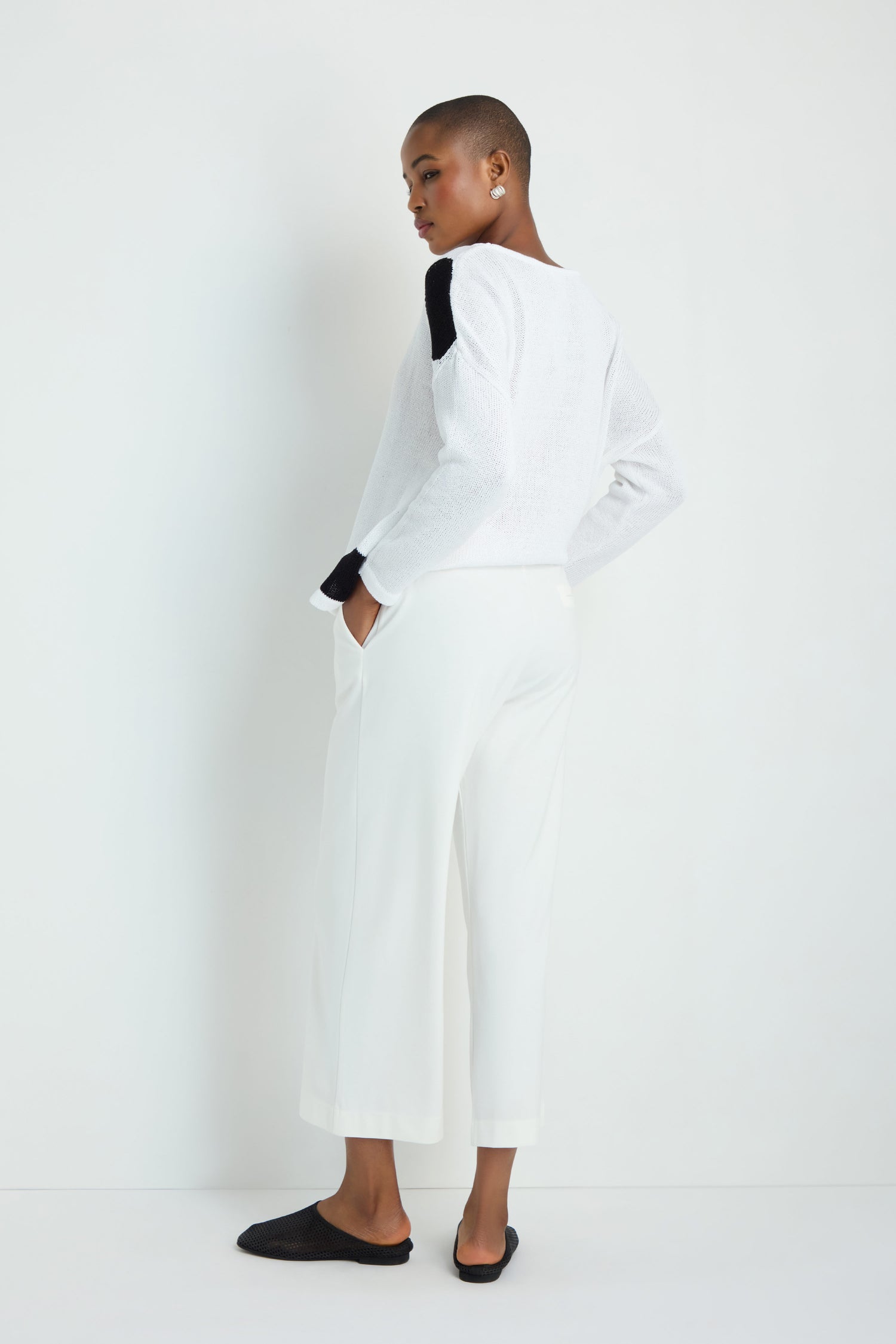A person with long gray hair faces away, wearing a loose-knit beige top and Wide Leg Pocket Trousers in white viscose stretch with an elasticated waist, paired with white sneakers against a plain white background.