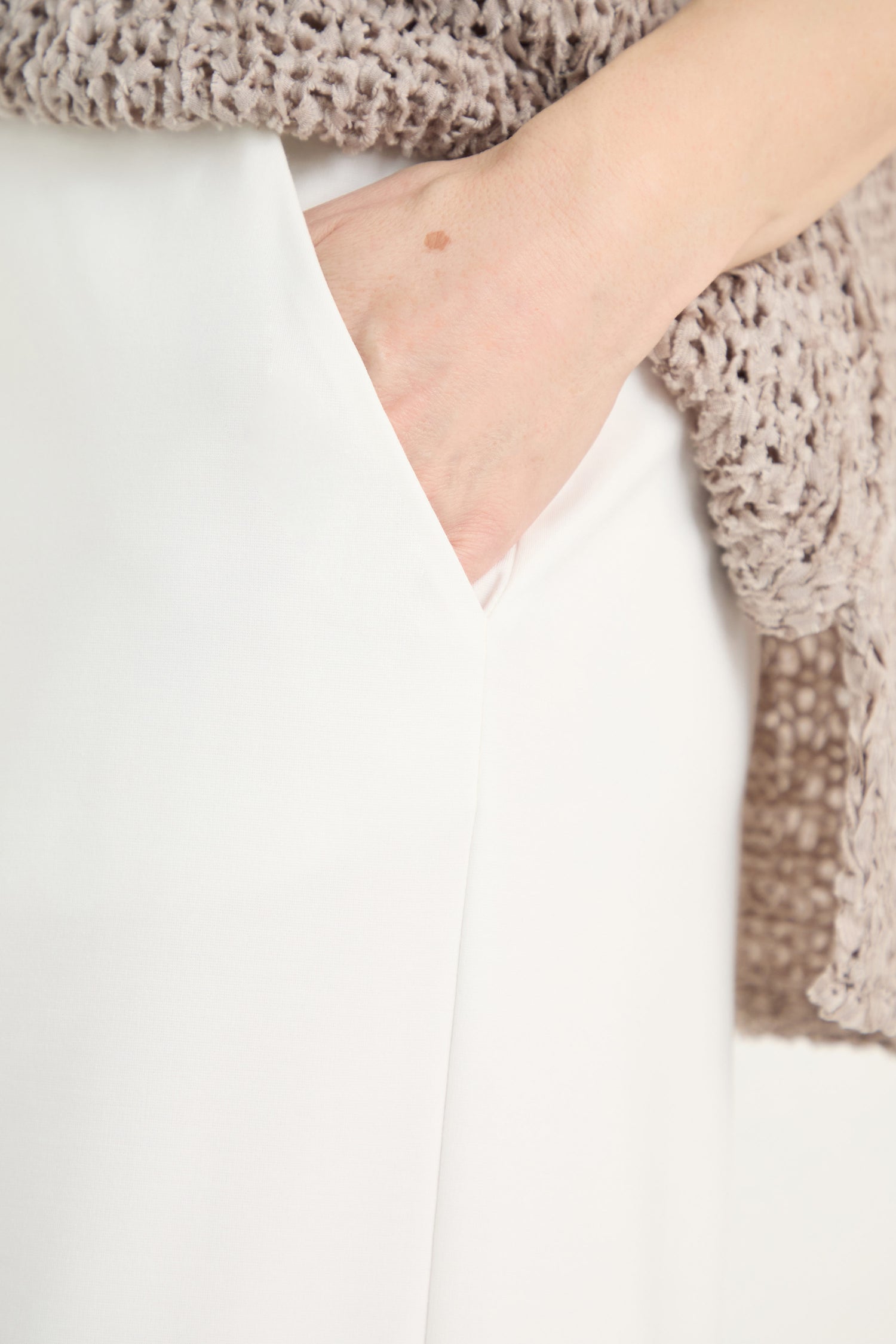 A person wearing Wide Leg Pocket Trousers in white with their hand in the pocket, partially covered by a textured beige sweater.