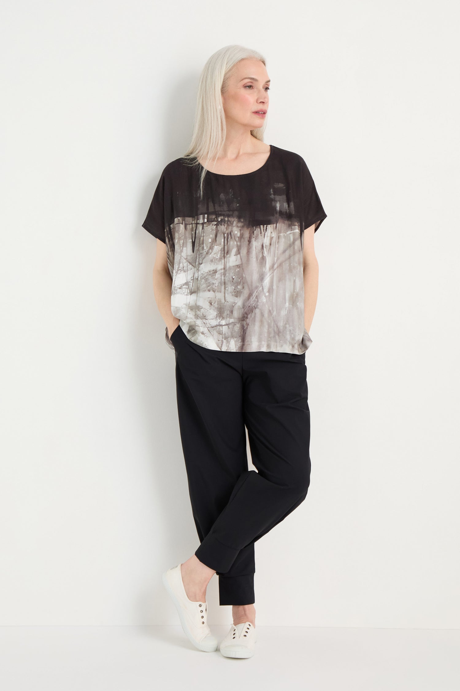 A woman with long gray hair wears the Abstract Print Easy Top with black pants and white sneakers, standing against a plain white background.