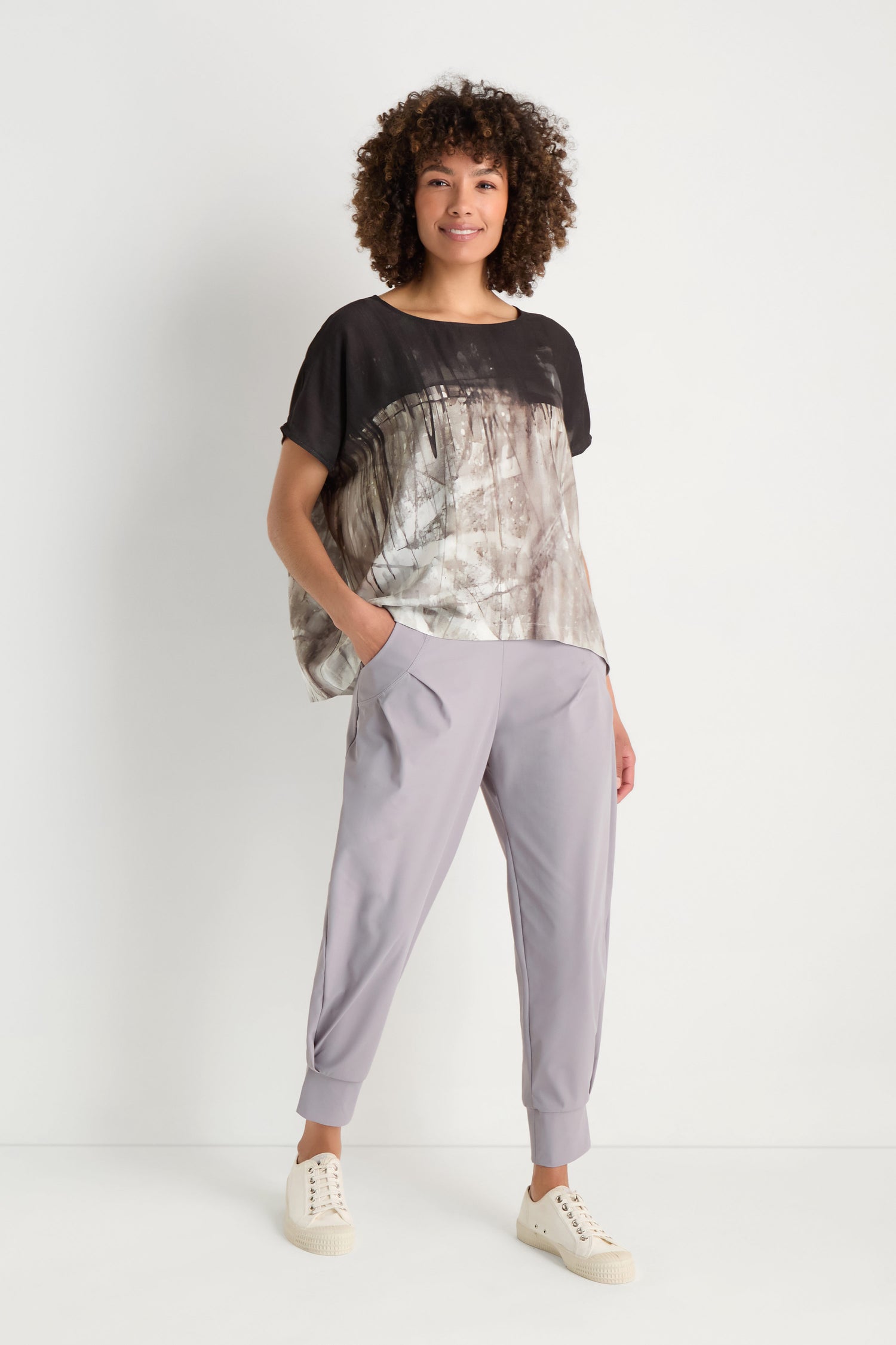 A woman with long gray hair wears the Abstract Print Easy Top with black pants and white sneakers, standing against a plain white background.