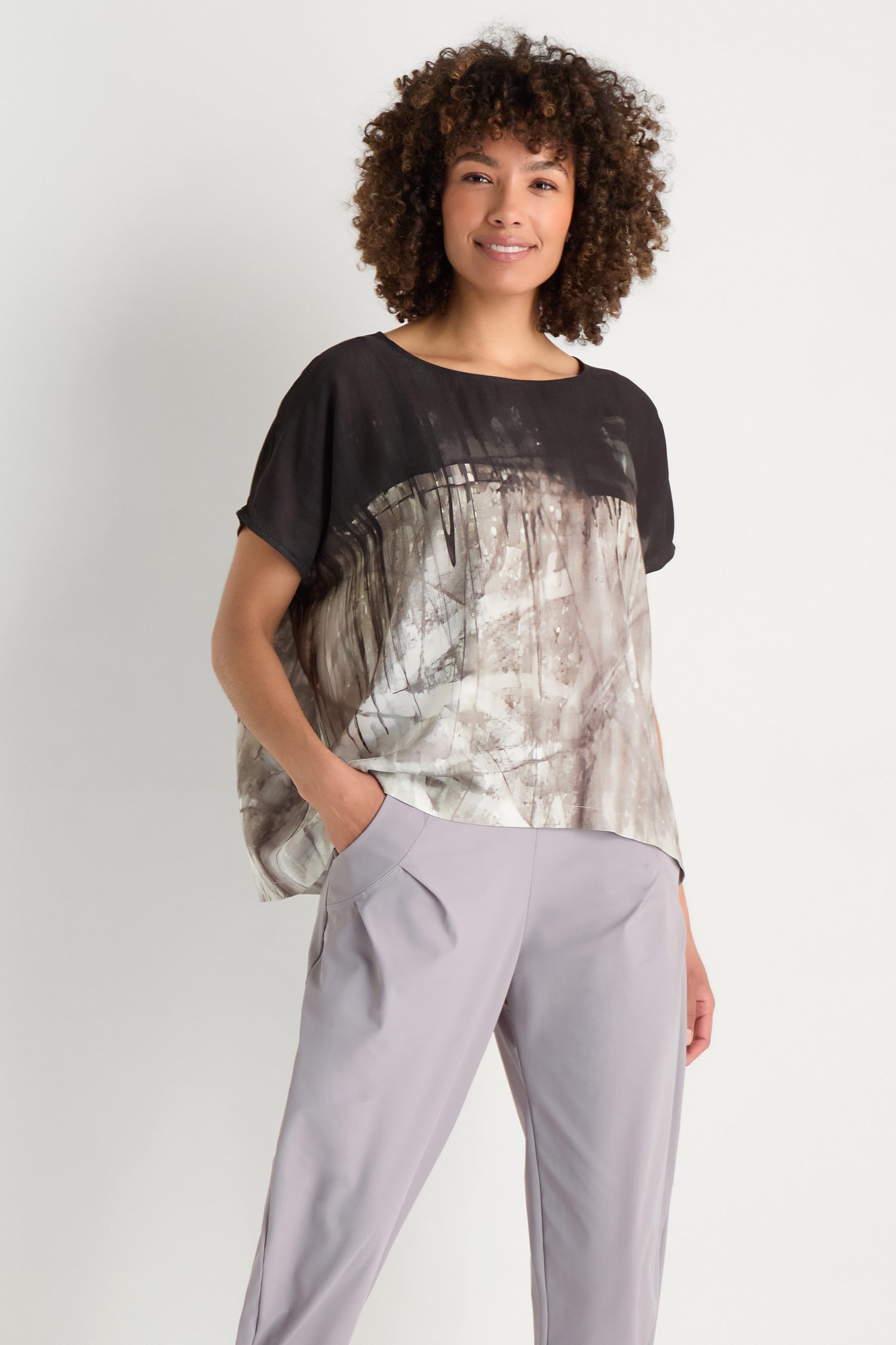 A woman with long gray hair wears the Abstract Print Easy Top in black and gray, smiling slightly while standing against a plain white background.