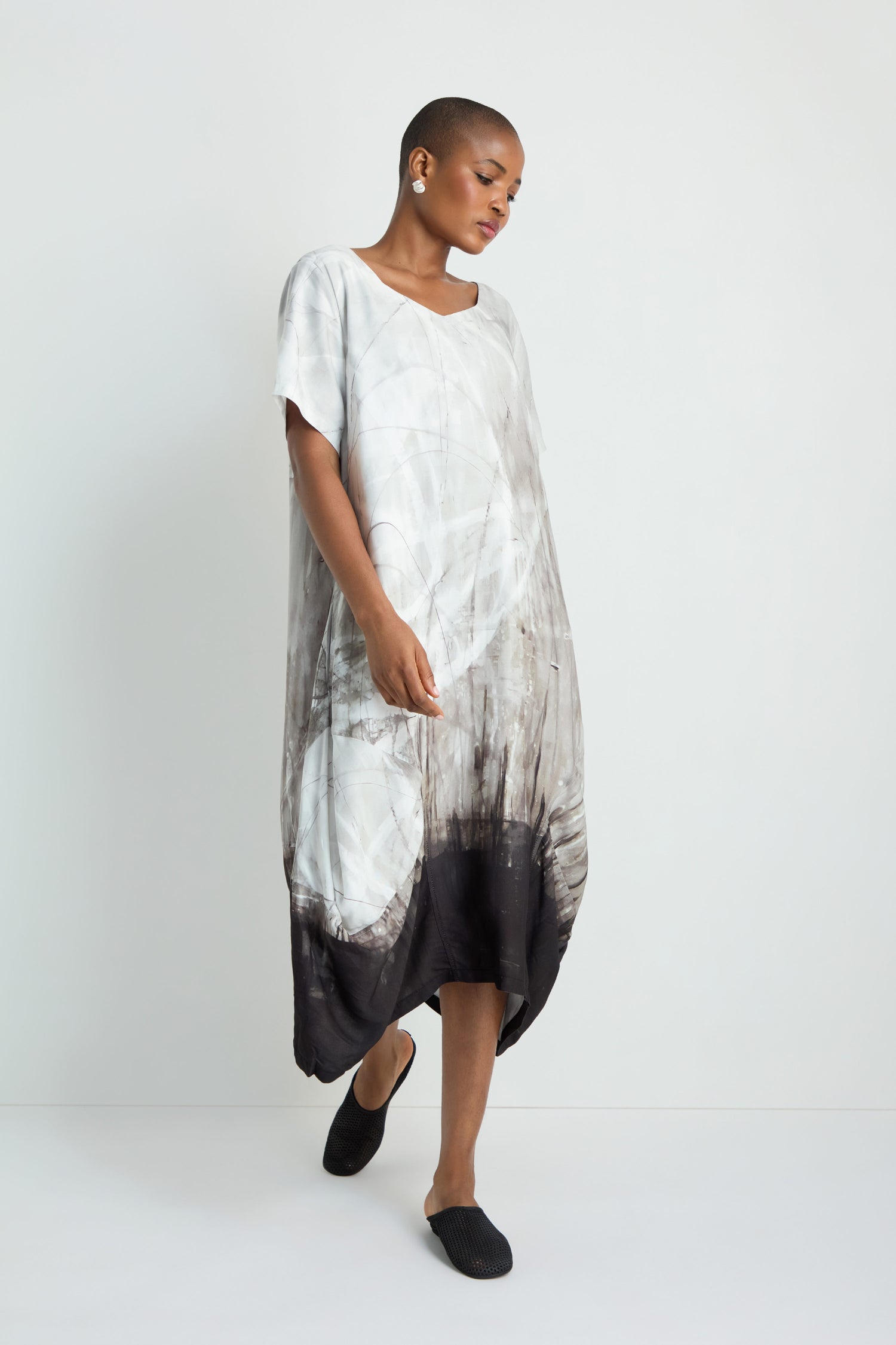 A woman with long white hair stands against a white background, wearing the Abstract Print Bubble Dress with an abstract gray and black pattern and black sandals.
