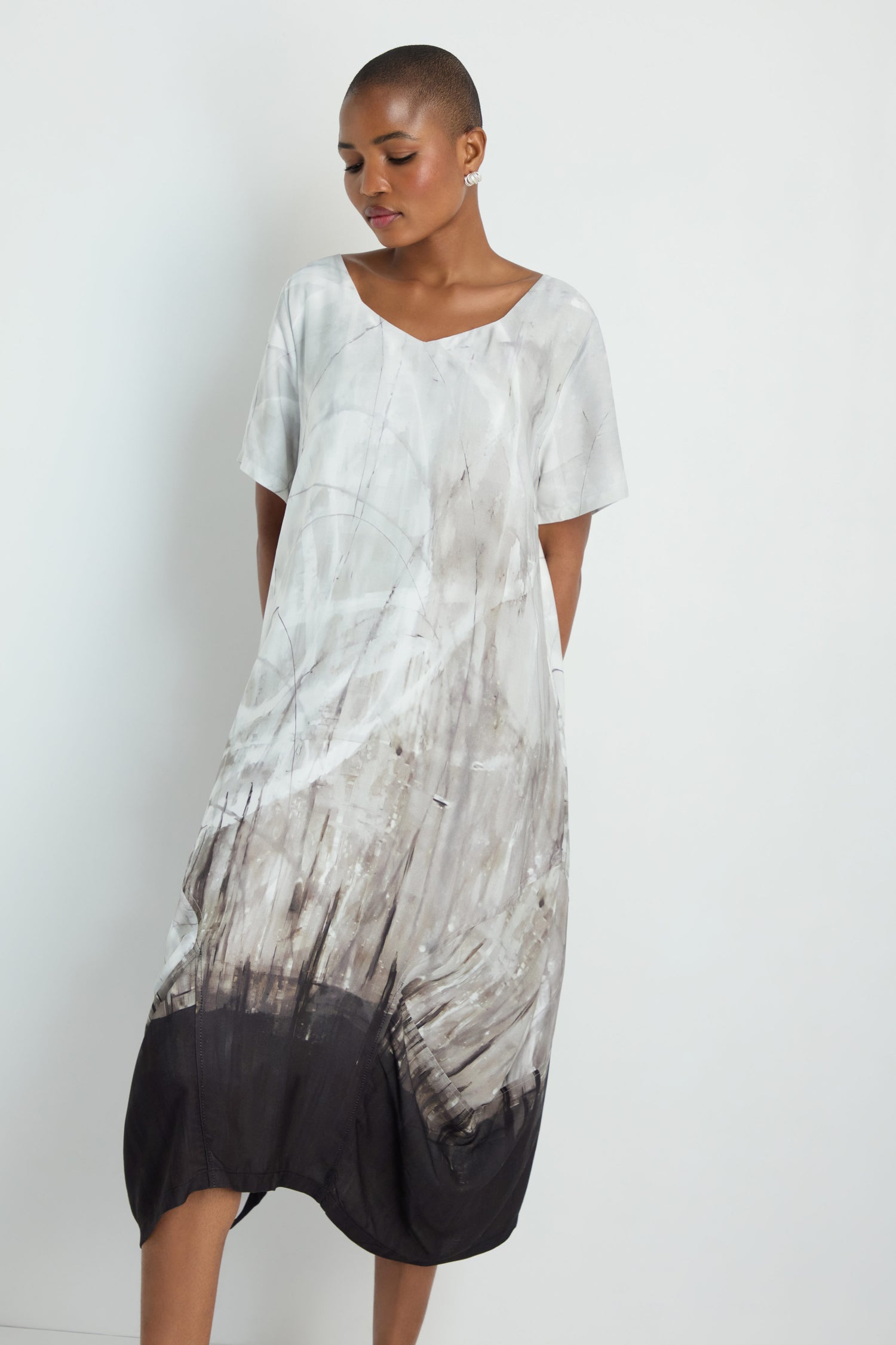 Woman with long gray hair wears the Abstract Print Bubble Dress, featuring a relaxed fit and a white, gray, and black abstract pattern, standing against a plain white background.