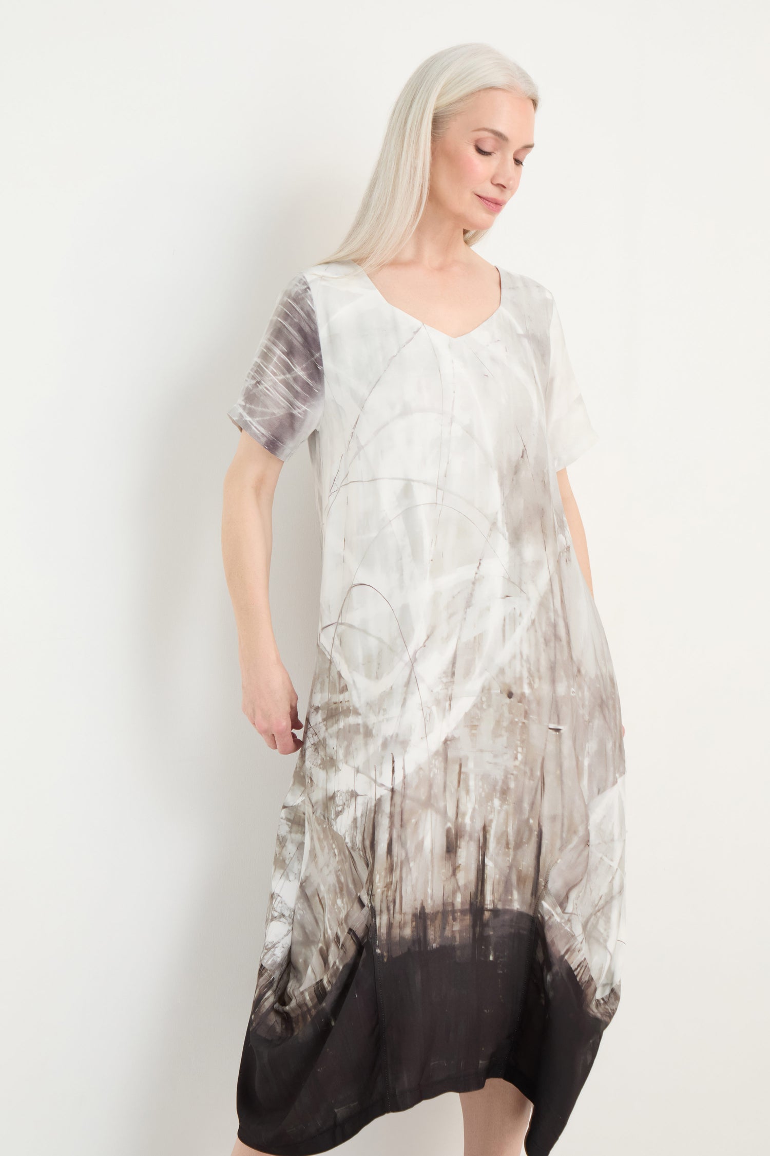 A woman with long white hair models the Abstract Print Bubble Dress, featuring a relaxed fit, short sleeves, and a gray-and-black abstract pattern, standing against a plain white background.