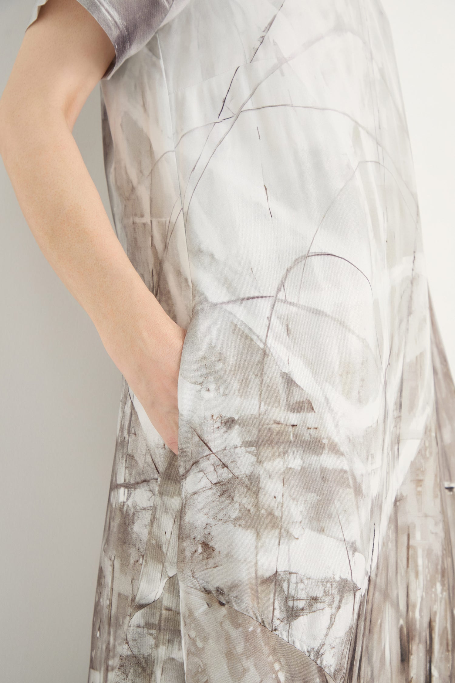 A person wearing the Abstract Print Bubble Dress, featuring a relaxed fit and an abstract light gray and brown pattern, has their right hand in a side pocket.