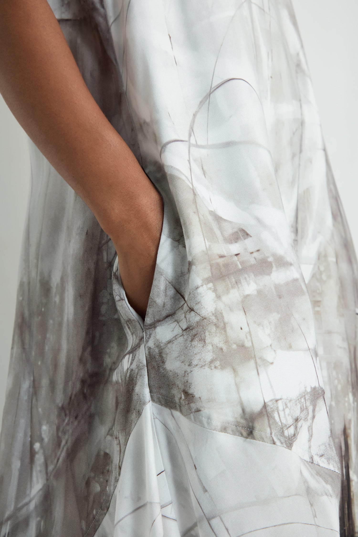 A person wearing the Abstract Print Bubble Dress, featuring a relaxed fit and an abstract light gray and brown pattern, has their right hand in a side pocket.