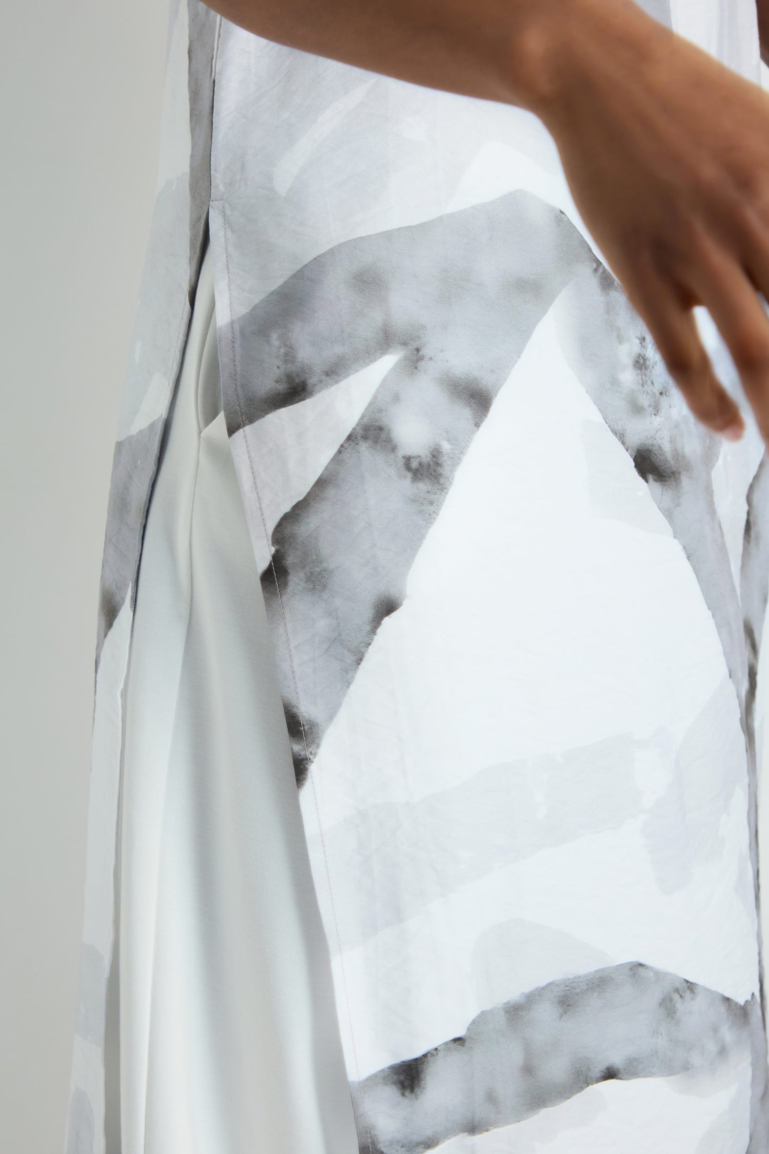 A woman with long gray hair models the Brushstroke Print Long Tunic featuring abstract black and gray patterns, paired with black pants and pearl earrings, standing against a plain light background.