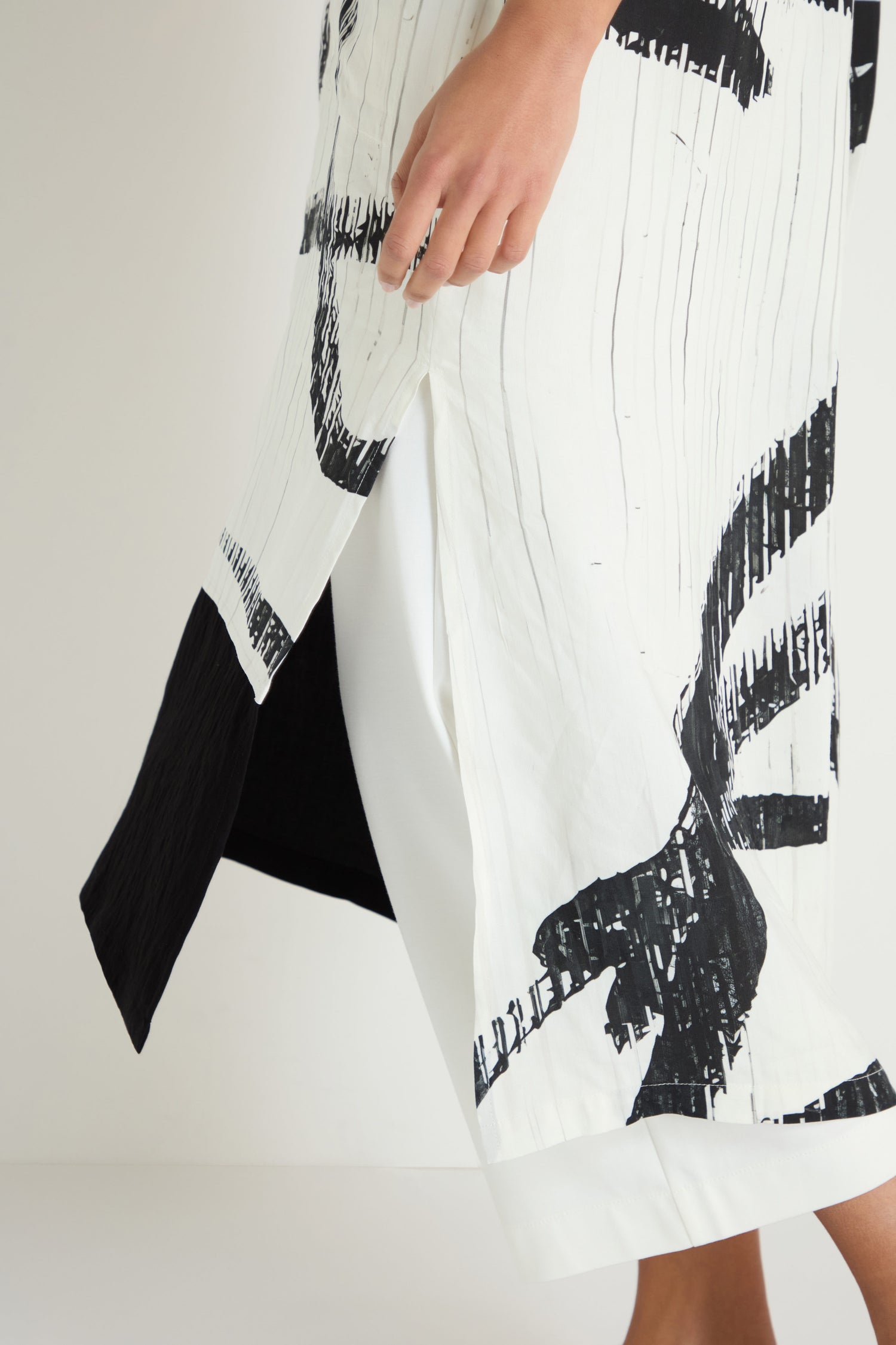 A person wearing the Soft Stripe Midi Dress, featuring a white, relaxed silhouette with black abstract patterns and a side slit, stands against a plain background.