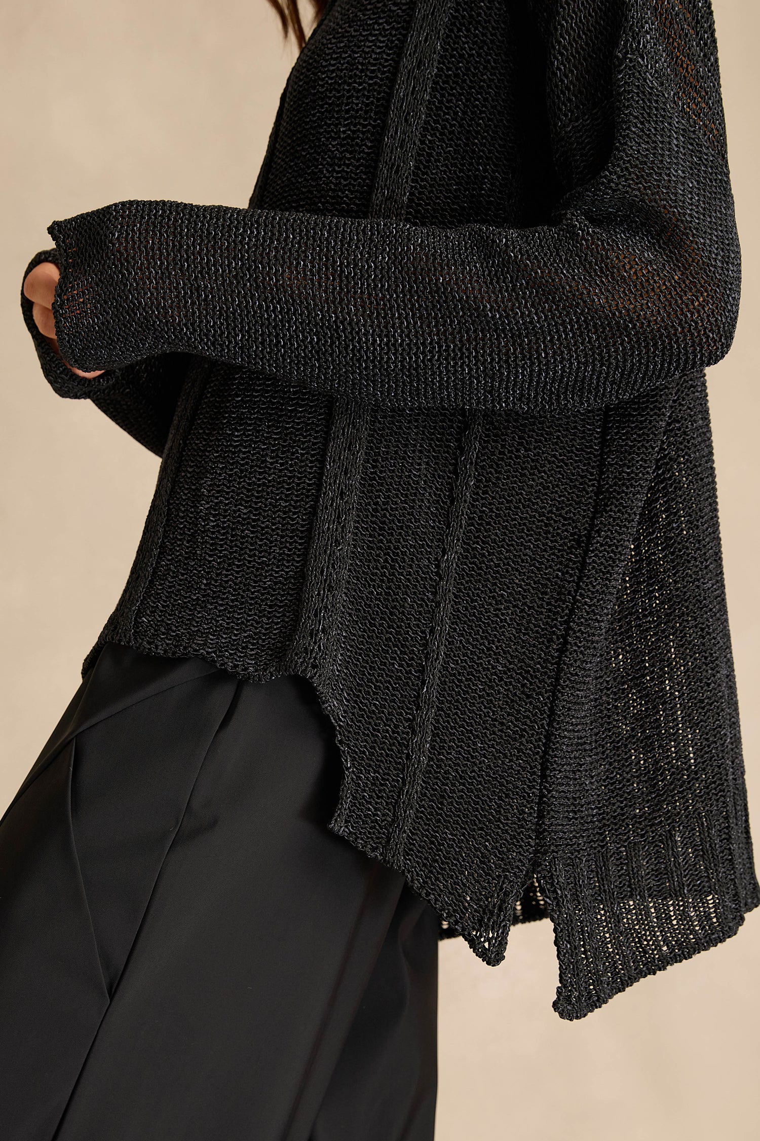 A person wears the Black Seam Detail Scoop Neck Knit – a longline black sweater with long sleeves – paired with black pants, shown from the shoulders to thigh against a neutral background. The cotton-rich knit offers a relaxed fit, adding both comfort and style to the overall look.