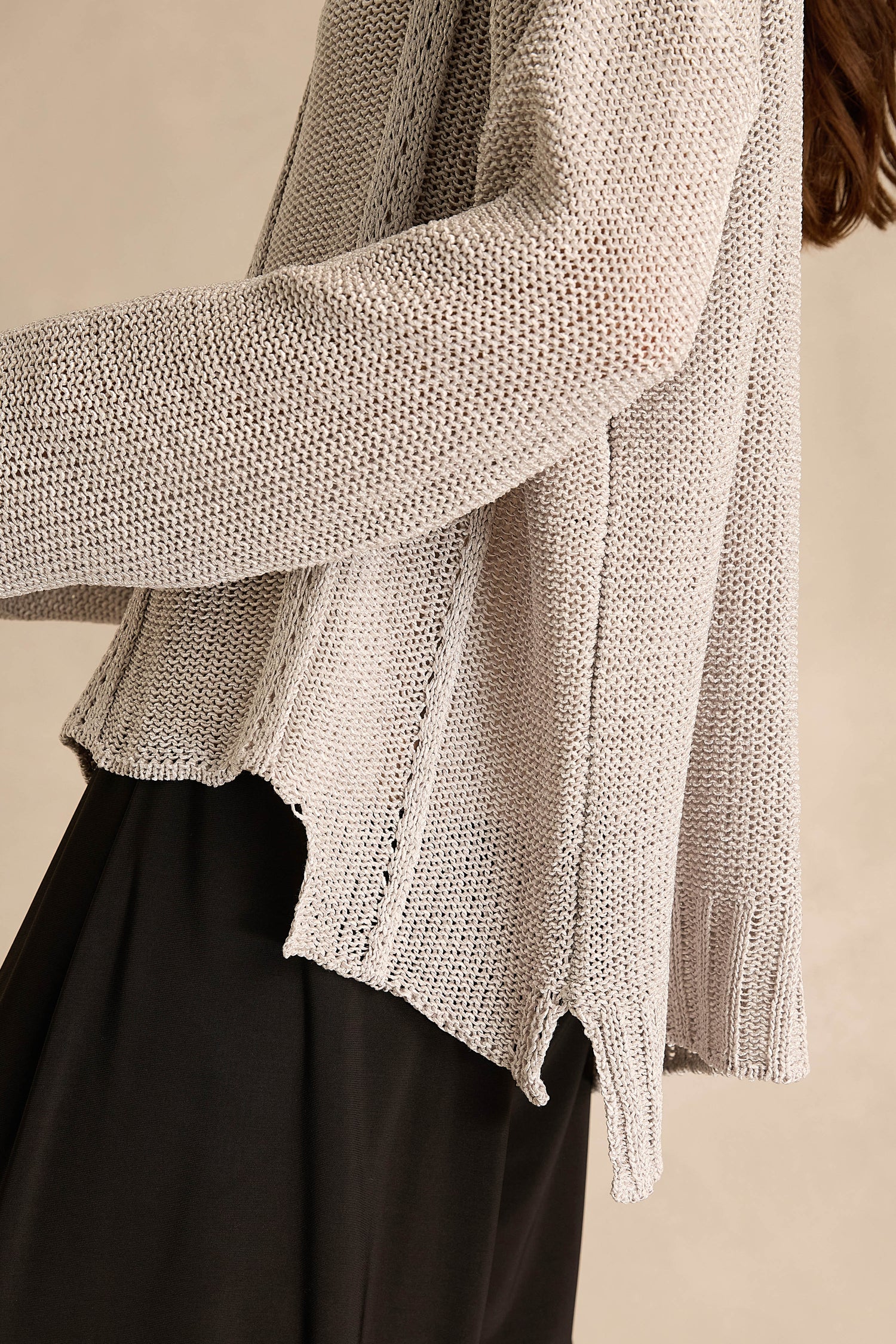 A person is shown from the shoulder down wearing the Silver Seam Detail Scoop Neck Knit—a loose-knit, light gray cotton-rich sweater featuring front seam detailing and side slits—paired with black pants.