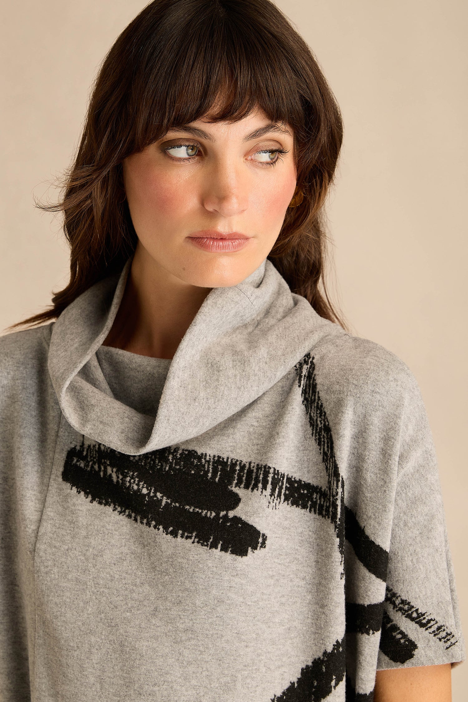 A woman with wavy brown hair wears the Paint Stripes Draped Neck Top—light gray with a bold black brushstroke motif—looking to her left against a neutral background.