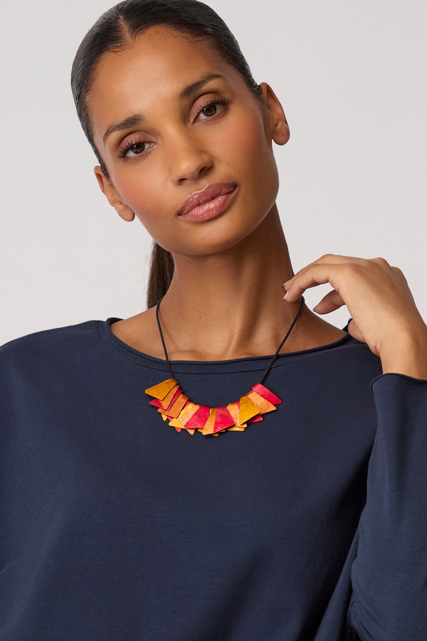 A person wearing a navy blue top and the Mini Segment Necklace poses for the camera, holding the contemporary piece in one hand.