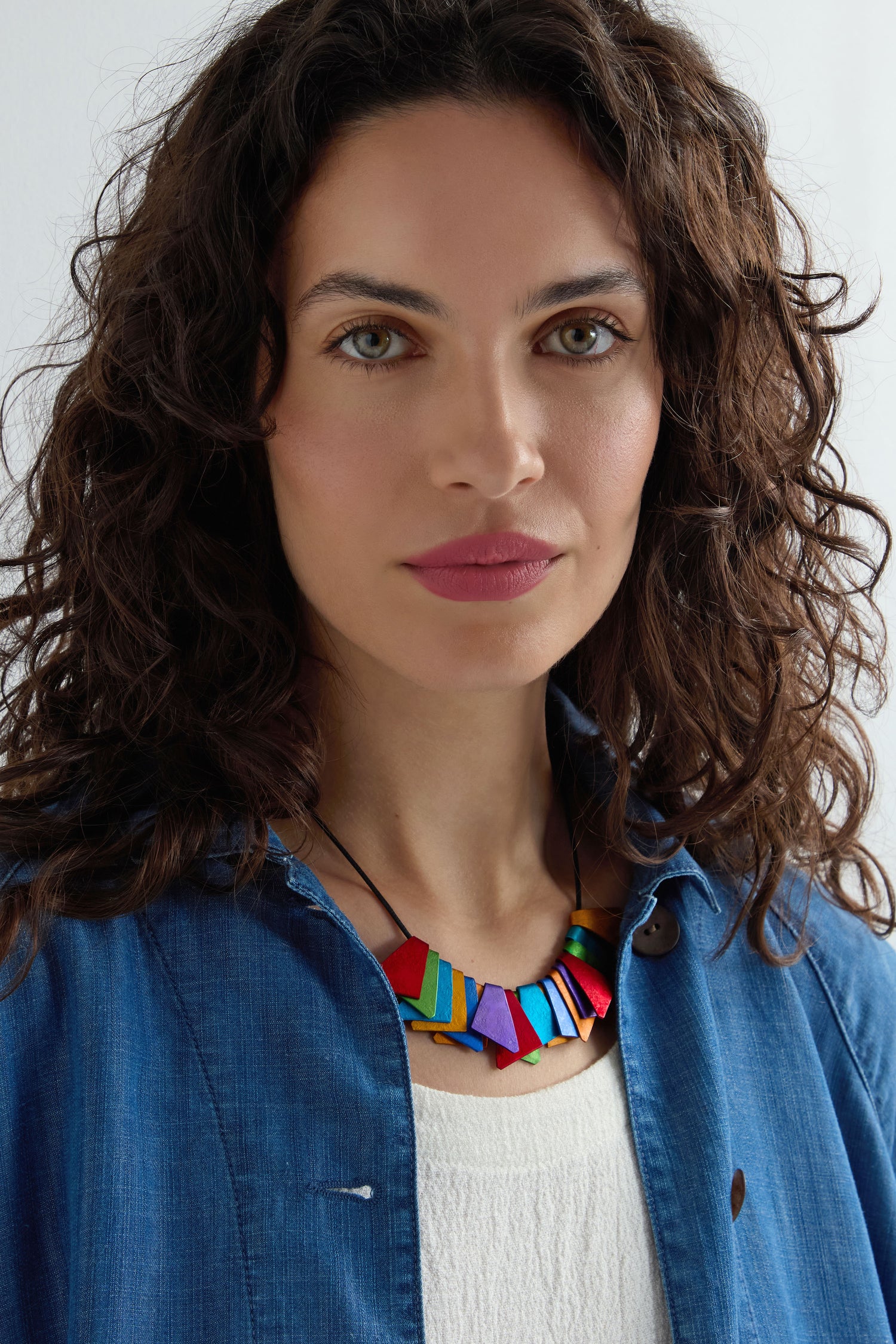 A woman with curly brown hair wears a blue shirt over a white top and the Mini Segment Necklace, looking directly at the camera.