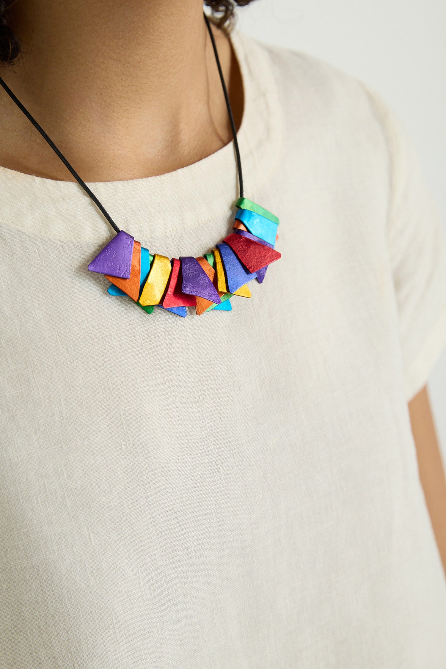 Close-up of a person wearing a cream-colored shirt and the Mini Segments Necklace—colorful, geometric-shaped beads on black cord.