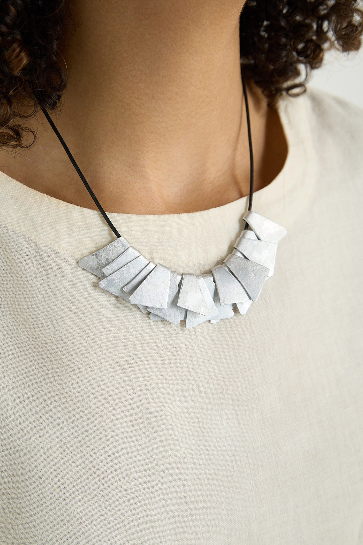 Close-up of a person wearing a cream-colored top and the Mini Segments Necklace—anodised aluminium triangles strung on a black cord.