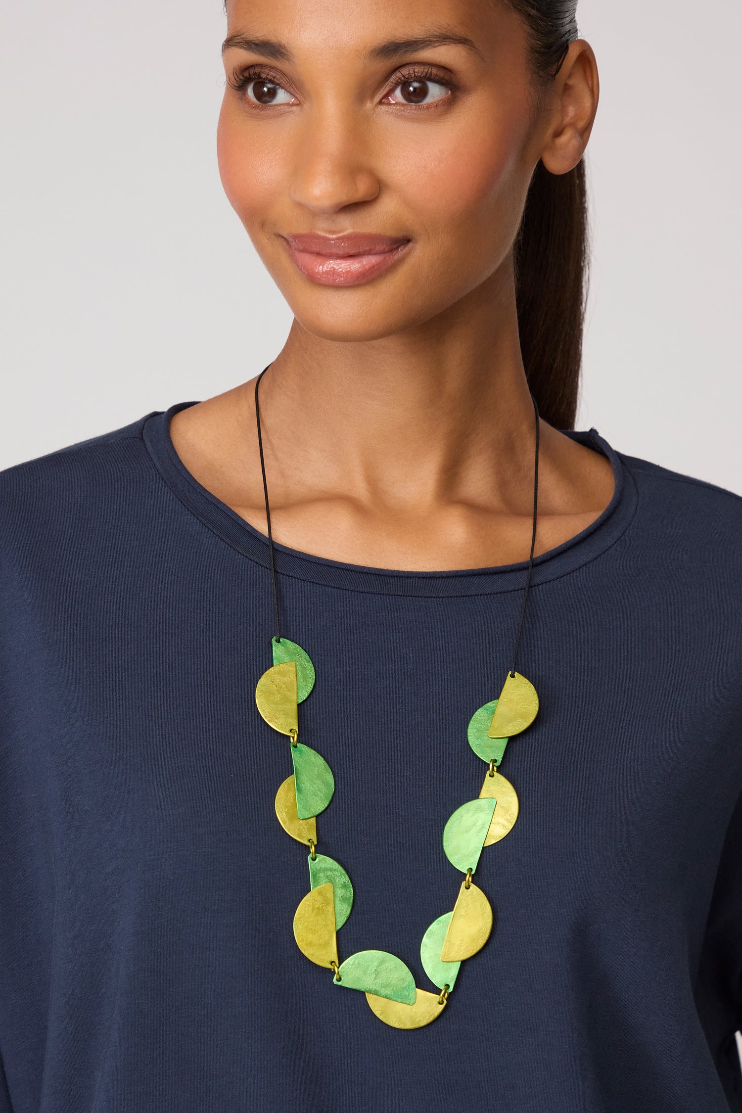 A woman wears a navy blue top and the Half Moon Necklace with large, flat, round green and yellow beads for a bold geometric style.