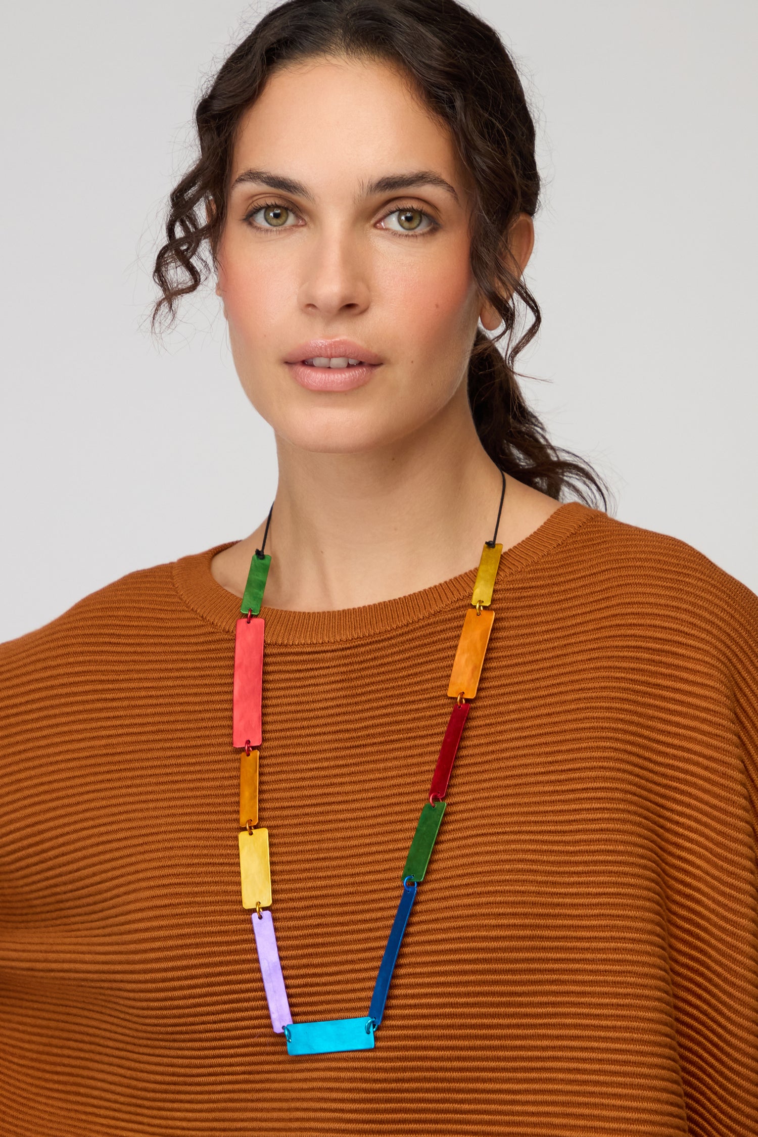 A woman poses against a plain background wearing a rust-textured top and the Colourful Rectangles Necklace, a contemporary statement piece with vibrant rectangular beads.