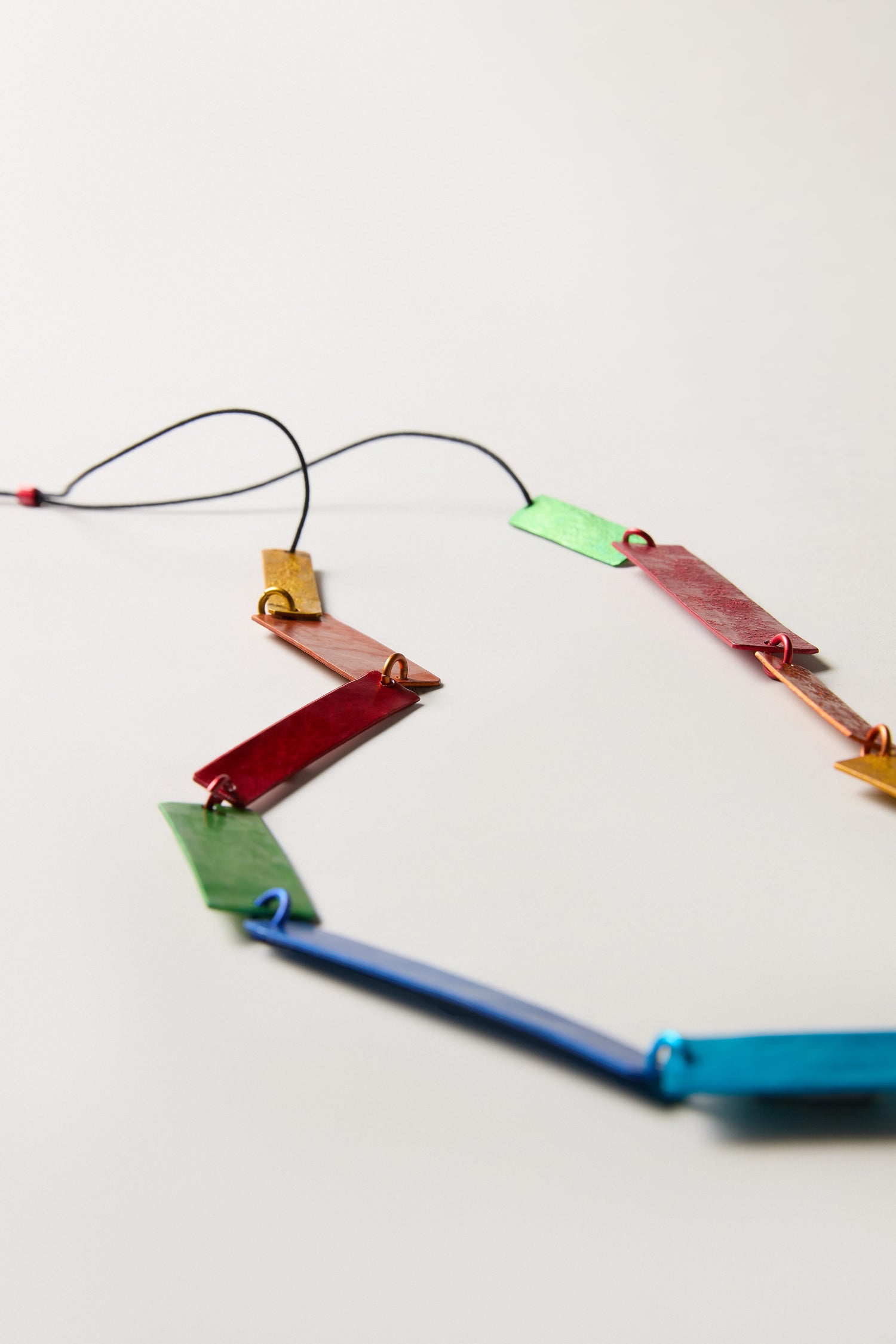 The Colourful Rectangles Necklace features sculptural, multicoloured rectangular metal pieces connected by wire, artfully displayed on a plain white surface.