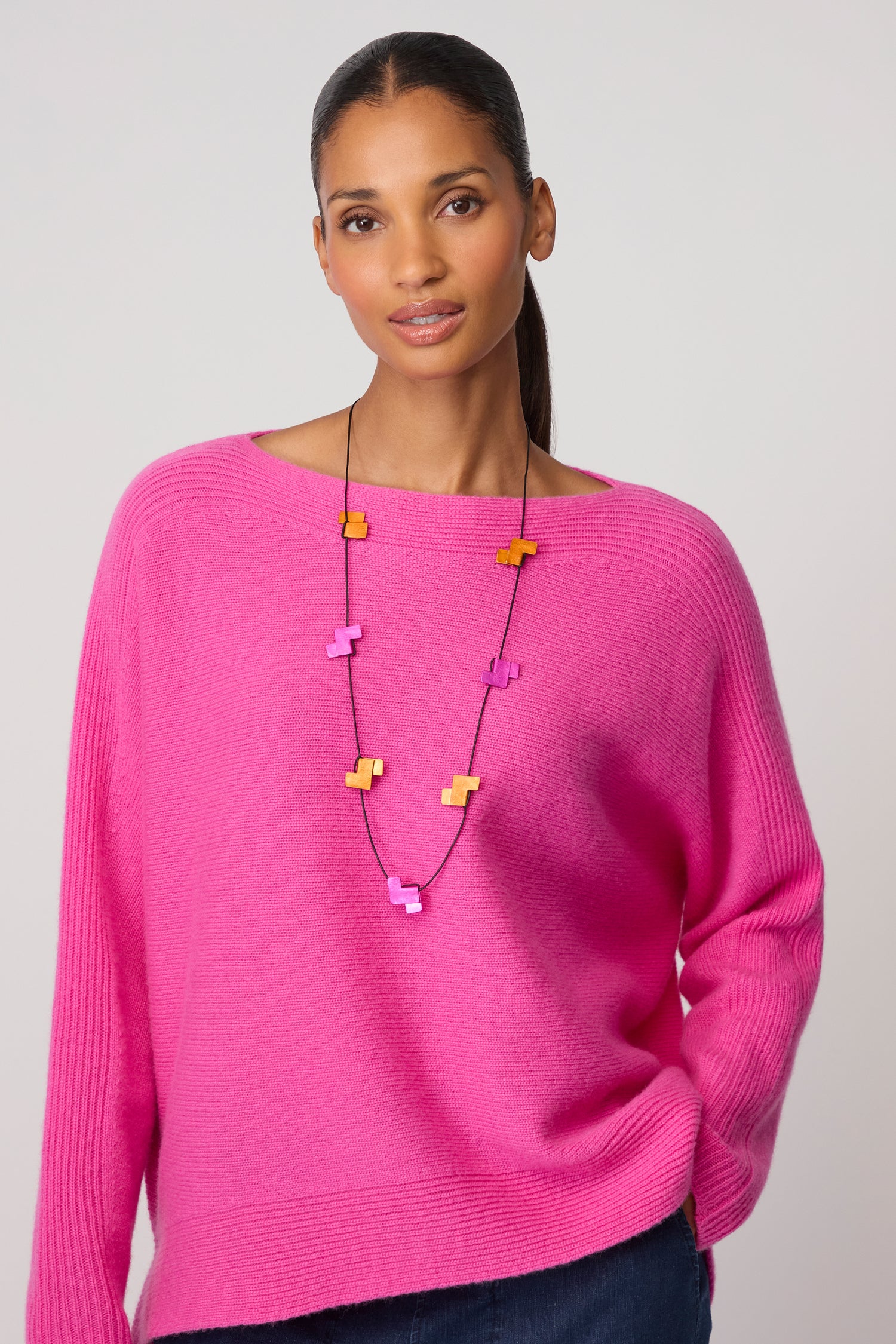 A woman in a bright pink sweater wears the Tetris Necklace, featuring bold pink and yellow geometric shapes, standing against a plain light background to showcase modern style.