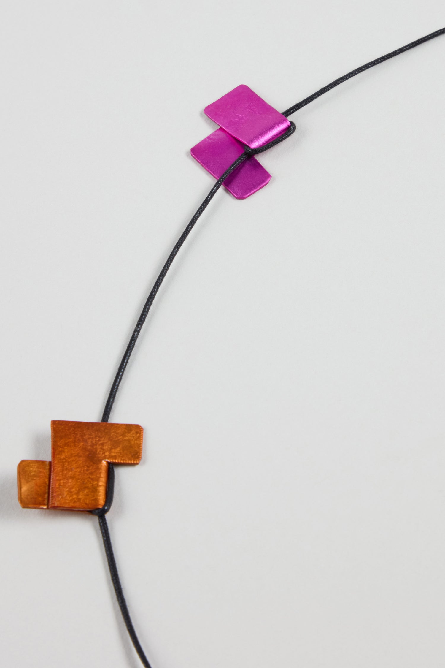 A thin black cord adorned with geometric copper and magenta metal pieces, the Tetris Necklace showcases bold contemporary style.