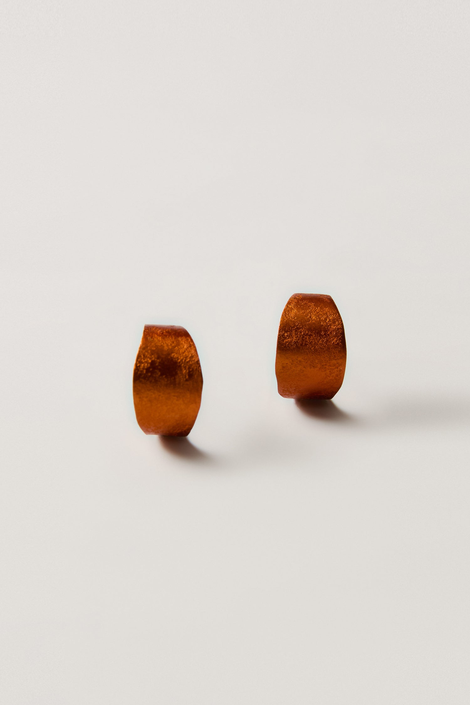 The Curved Earrings are small, metallic, copper-colored geometric studs—perfect contemporary jewelry for anyone who loves subtle statement accessories.