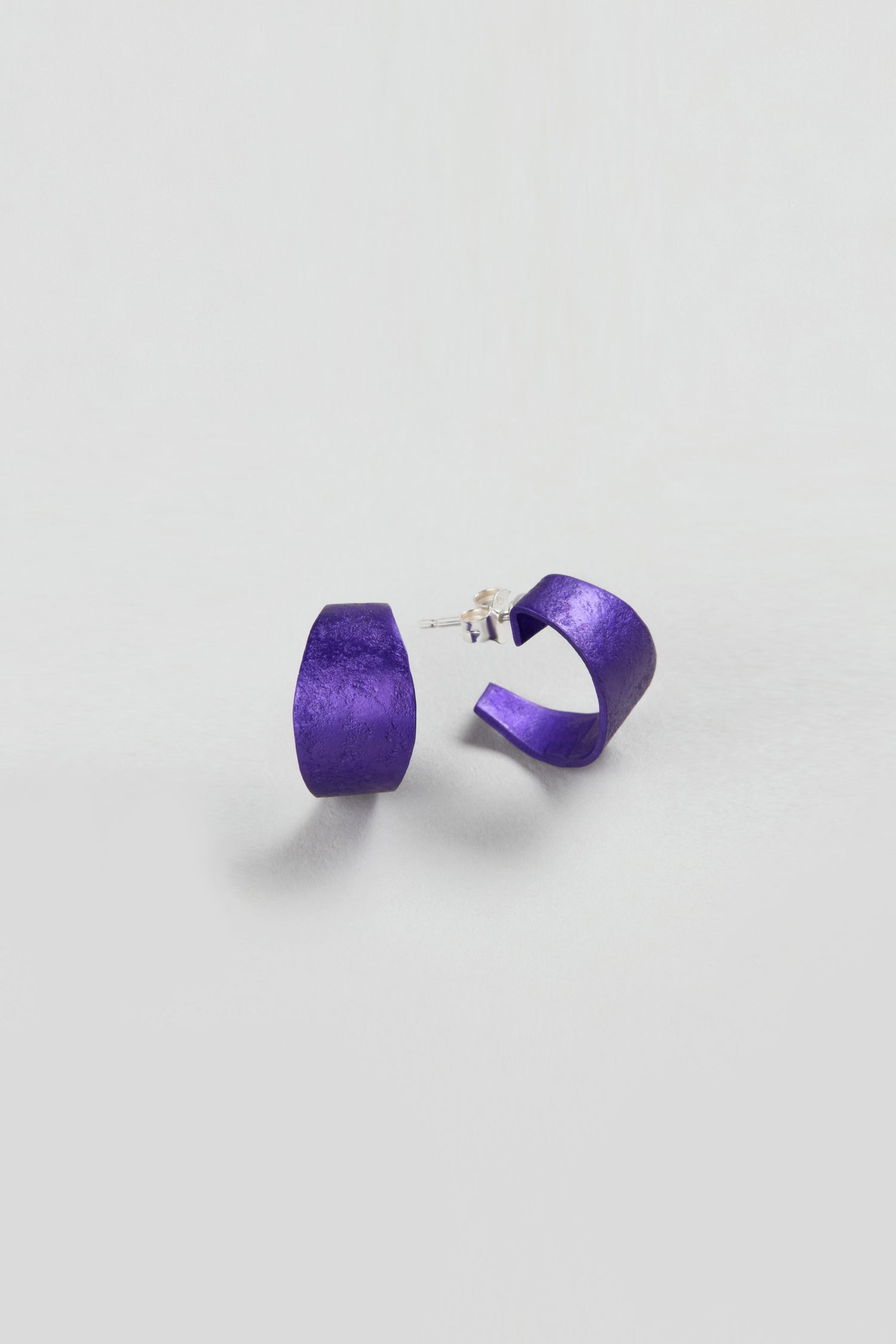 A pair of Curved Earrings in matte purple, ideal as statement accessories, showcased against a plain white background.