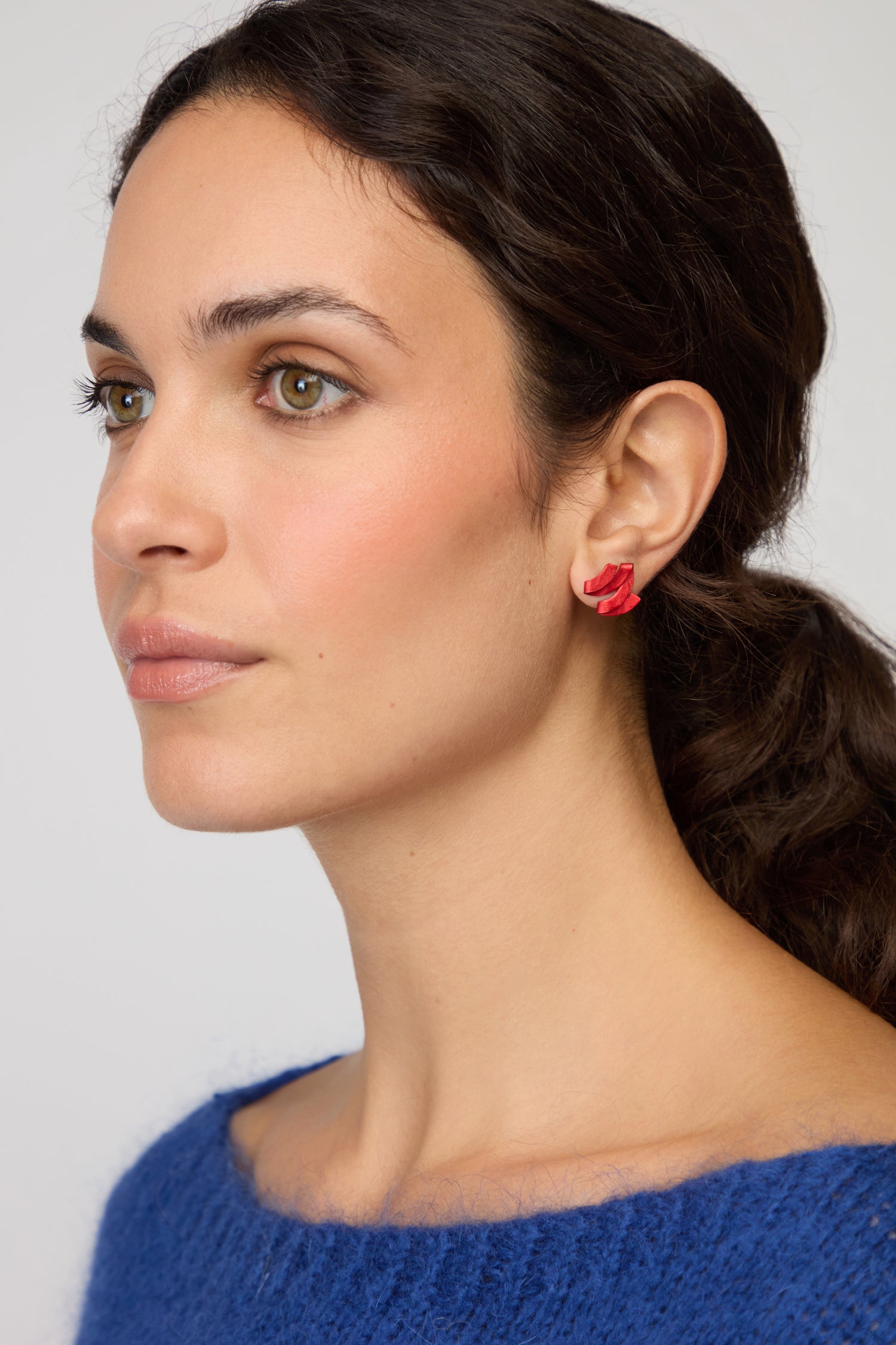 Woman with wavy dark hair wears a blue sweater and Ribbon Earrings—sculptural jewelry—gazing slightly to the side against a neutral backdrop.