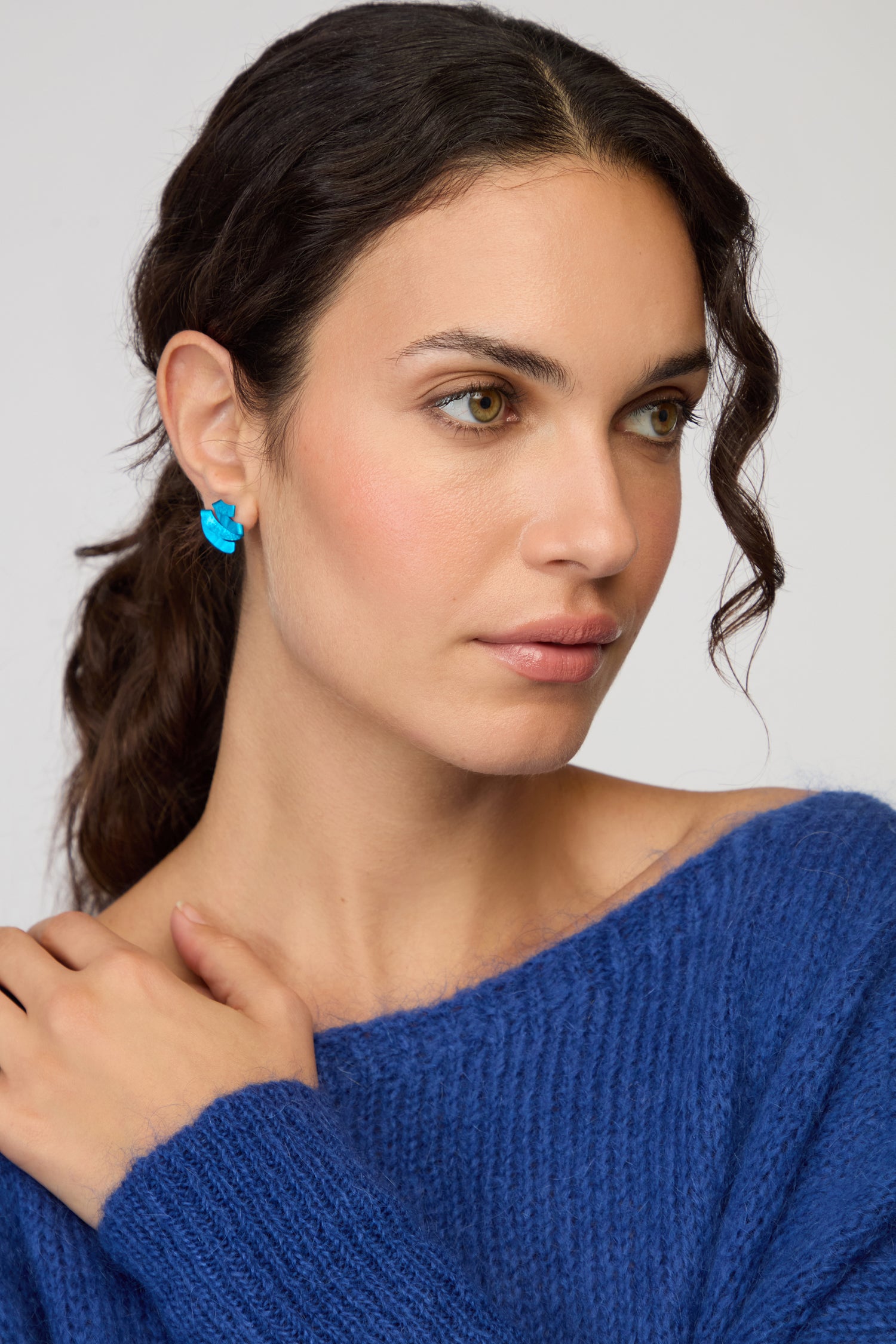 Woman with long dark hair in a ponytail wears a blue knit sweater and Ribbon Earrings, gazing slightly to the side with a neutral expression.