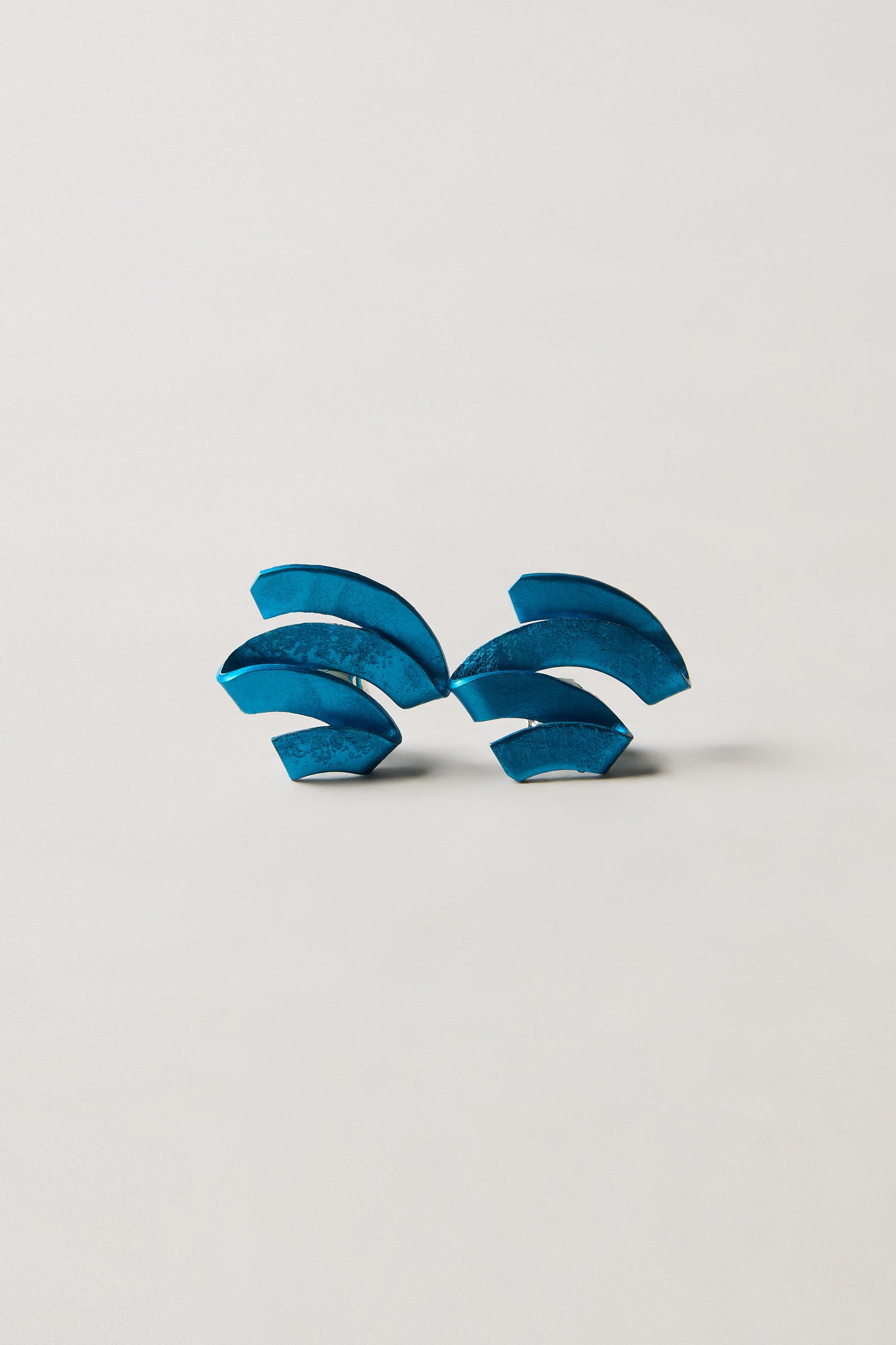 A pair of Ribbon Earrings crafted from geometric blue anodised aluminium, inspired by sculptural jewellery, showcased on a simple light background.