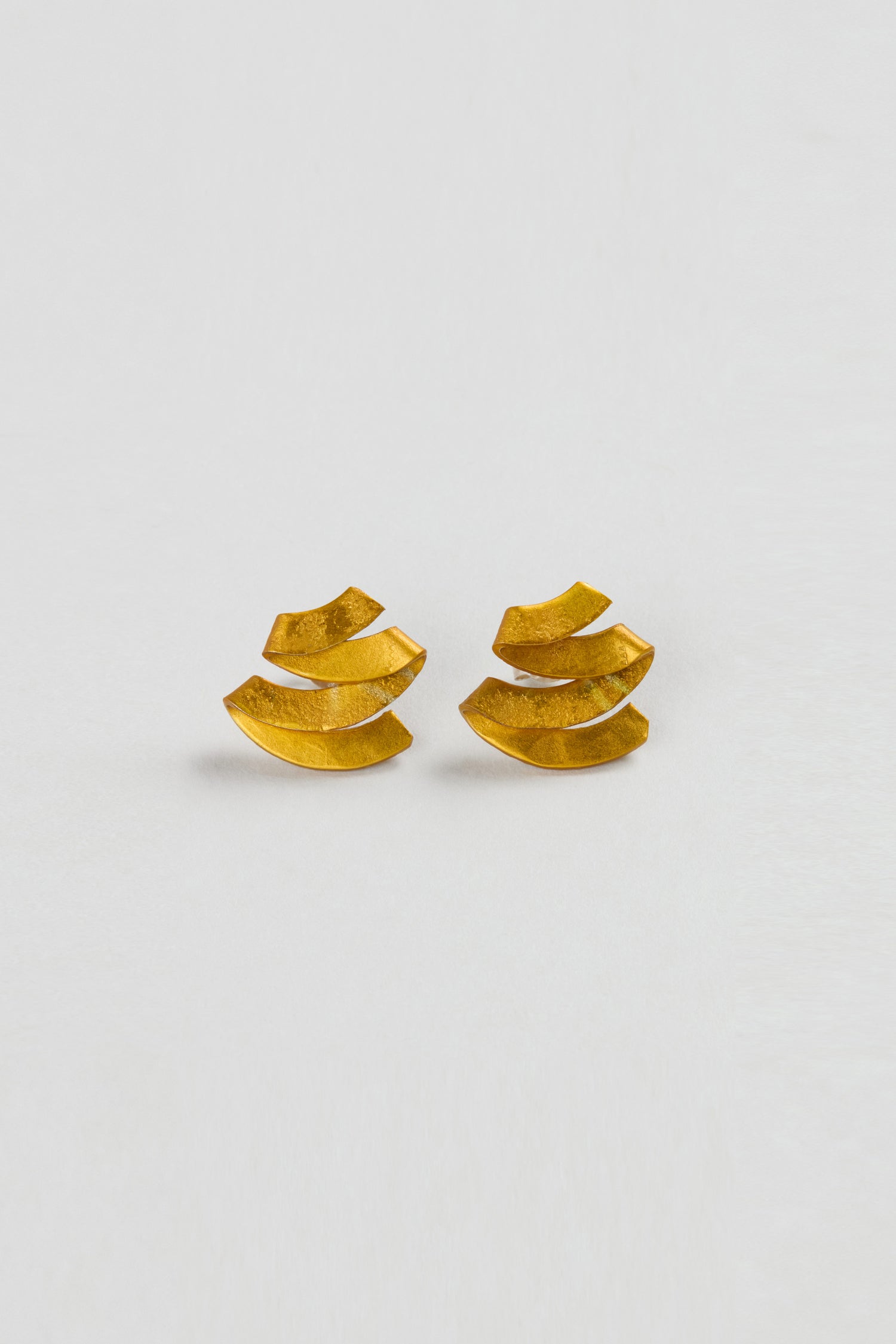 Ribbon Earrings: Gold sculptural earrings featuring a layered, curved design, displayed on a plain white background.