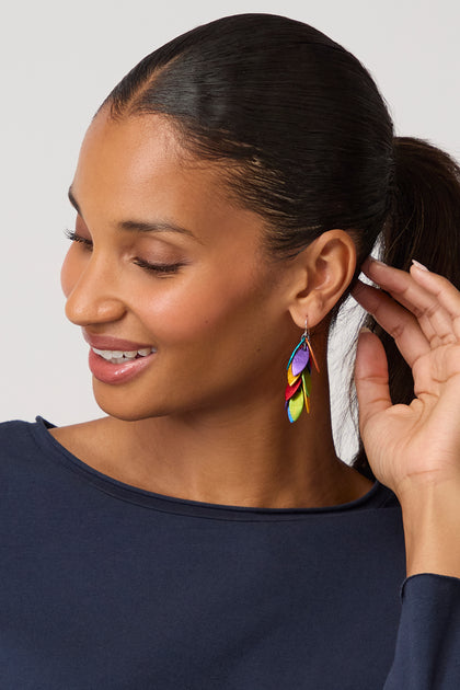 Smiling woman with a ponytail wears a navy top and Rainbow Scattered Leaves Earrings, touching her ear and looking down while showcasing her love for contemporary jewellery.