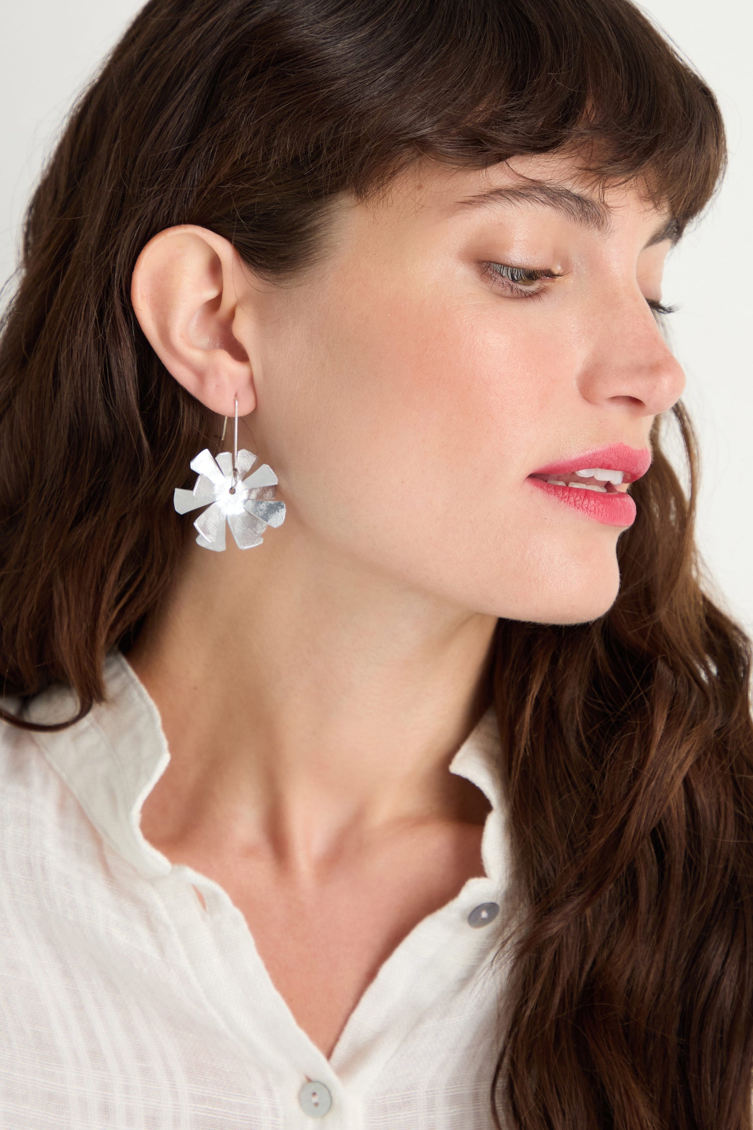 A woman models Flower Earrings—large florals with sterling silver hooks—paired with a white blouse, looking to the side against a plain background.