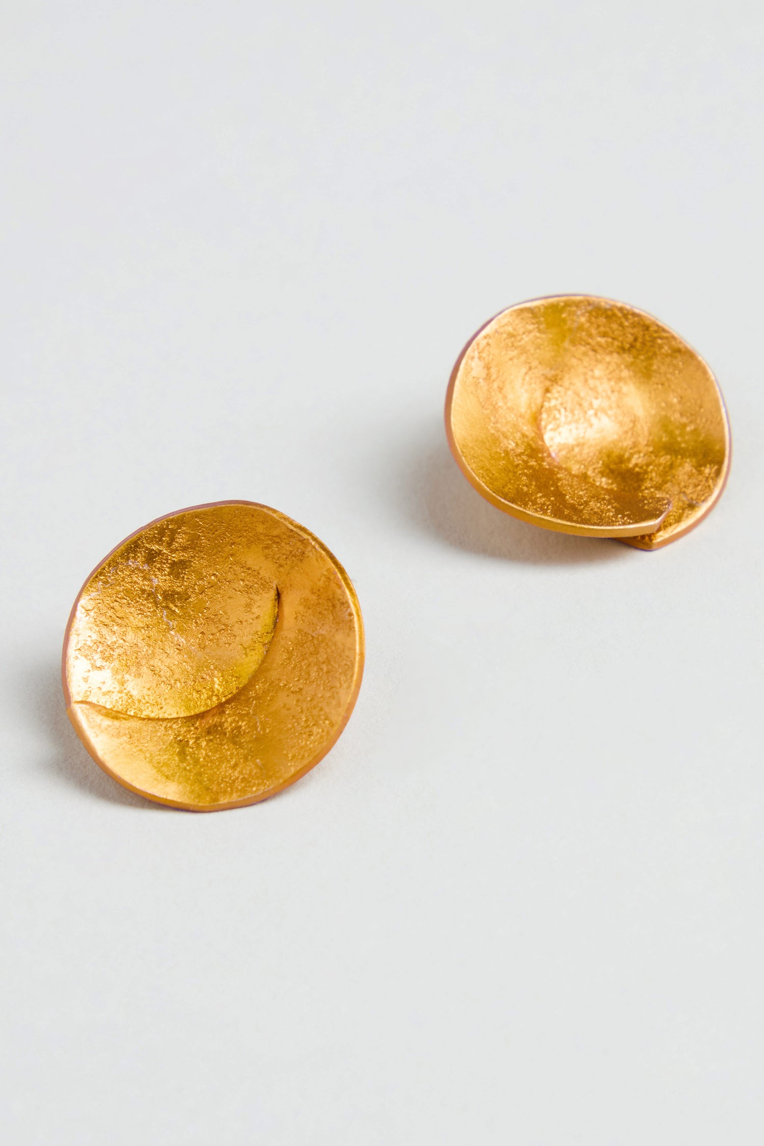 A pair of Curved Disc Earrings featuring round, textured gold discs and sterling silver posts, shown on a plain white background.