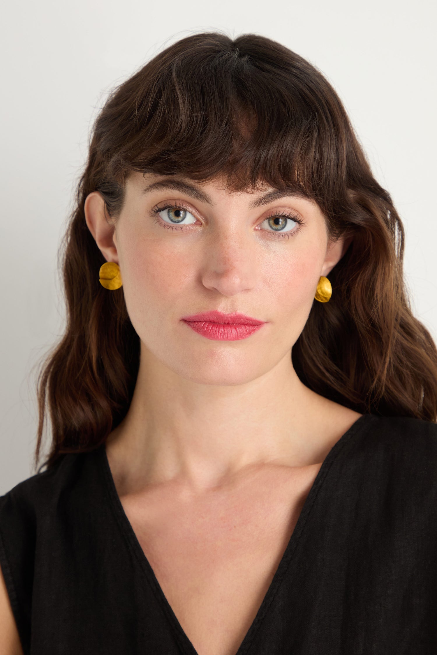 A woman with wavy brown hair and blue eyes wears Curved Disc Earrings with sterling silver posts and a black top, looking at the camera against a plain background.