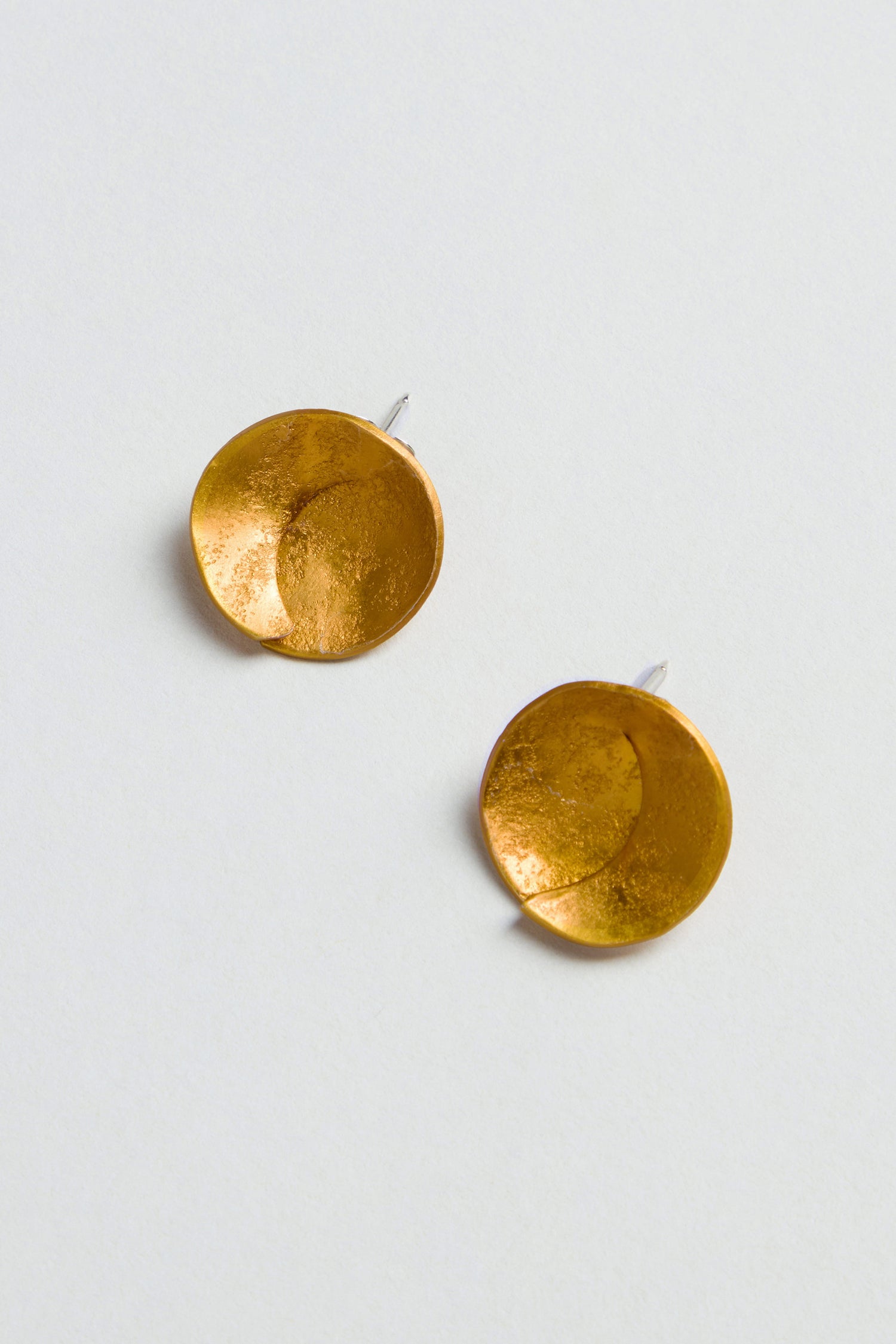 The Curved Disc Earrings feature a round, gold-toned, textured, overlapping design and are finished with secure sterling silver posts. Displayed against a light background.