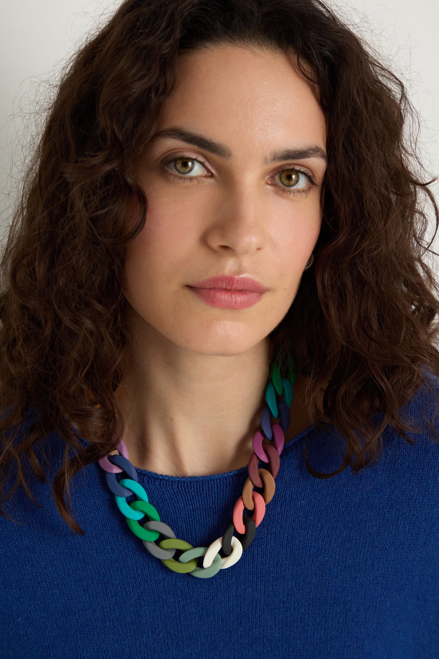 A woman with curly brown hair wears a blue top and the Colour Pop Link Necklace, its bold, chunky links standing out as she looks straight at the camera against a plain background.