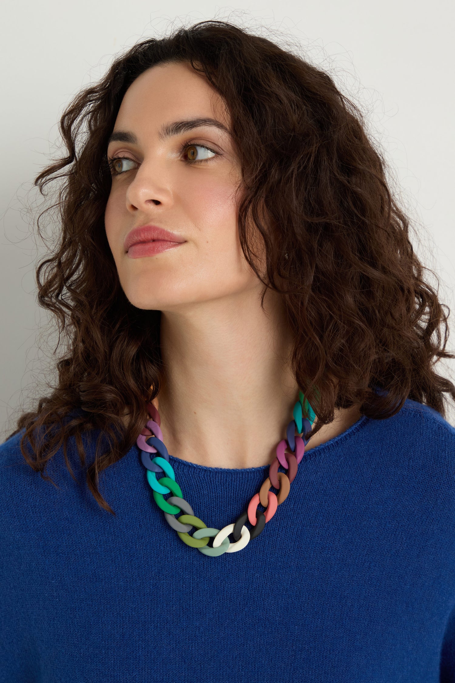 A woman with curly brown hair, in a blue sweater, wears the Colour Pop Link Necklace—featuring chunky links—as she looks to the side against a plain background.