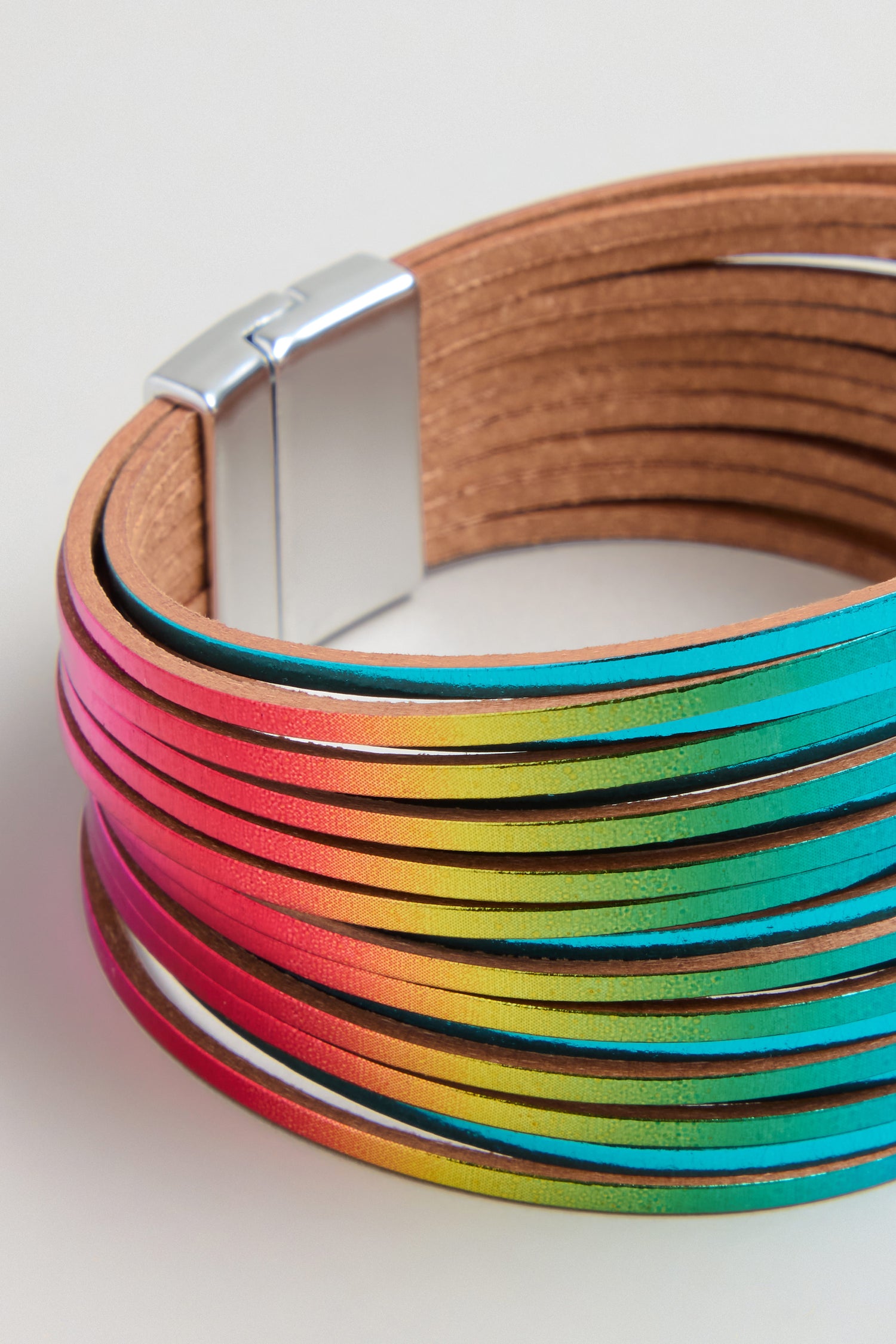 The Vegan Leather Metallic Bracelet features multi-strand vegan leather in a gradient rainbow design with a silver magnetic clasp, making it a lightweight accessory that adds vibrant color to any outfit.
