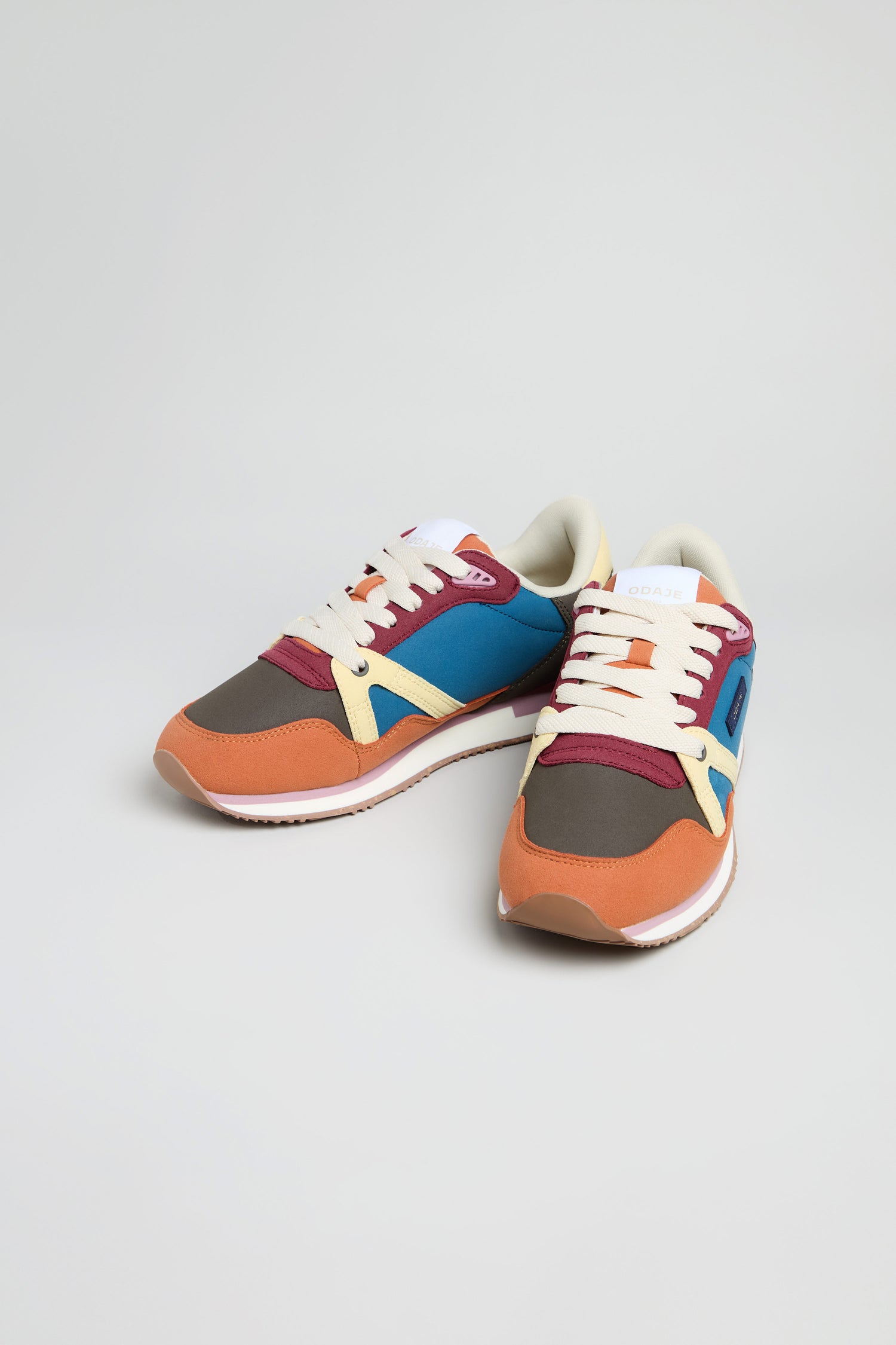 The Colour Pop Andree Trainers are vibrant vegan shoes with orange, blue, maroon, yellow, and brown panels, plus white laces and soles, shown on a plain light background.