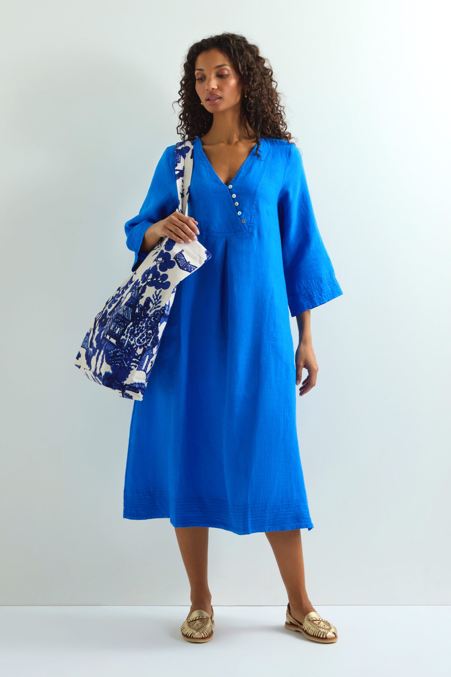 A person in a blue dress holds the Willow Canvas Bag, made from sustainable cotton with a willow design, against a plain backdrop.