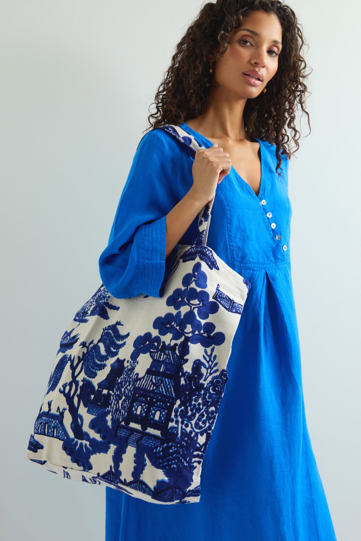 A person in a blue dress holds a Willow Canvas Bag, crafted from sustainable cotton with an elegant design.