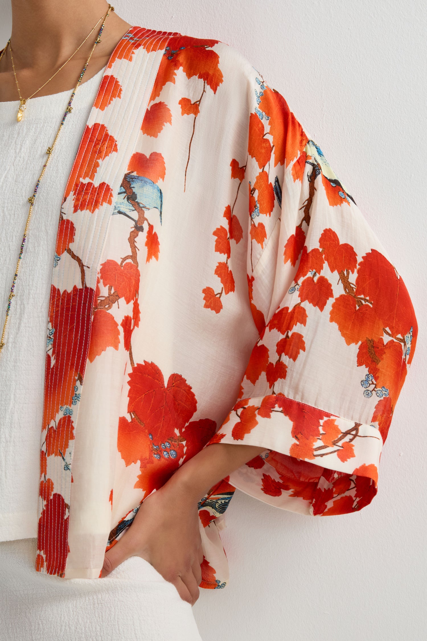 A person wears the Acer Print Kimono, a cream kimono with summer prints of red and orange birds and Japanese maple trees, styled over a white outfit against a plain light background.