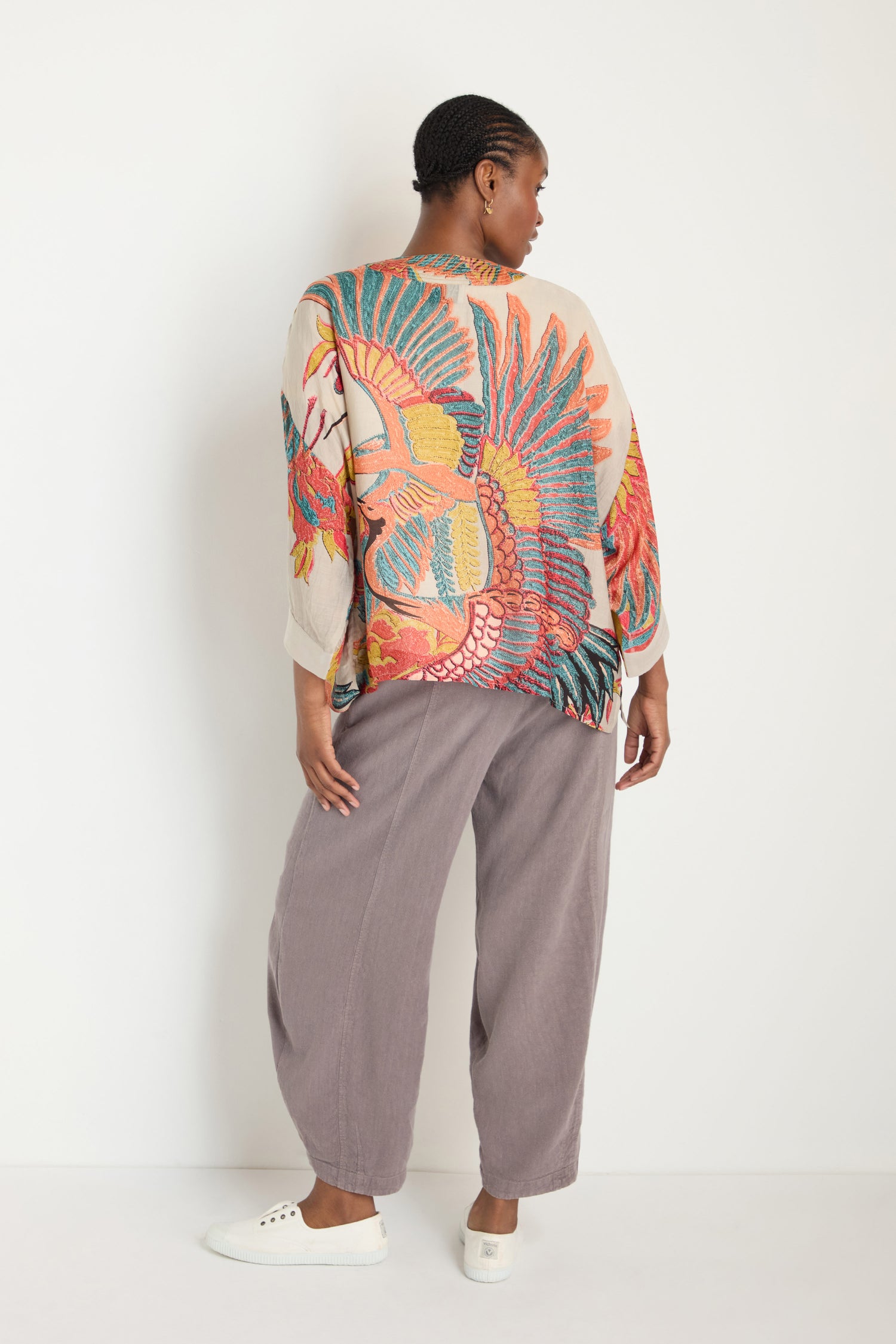 A person stands facing away, wearing the Crane Stone Print Kimono with timeless prints, loose gray pants, and white sneakers against a plain white background.