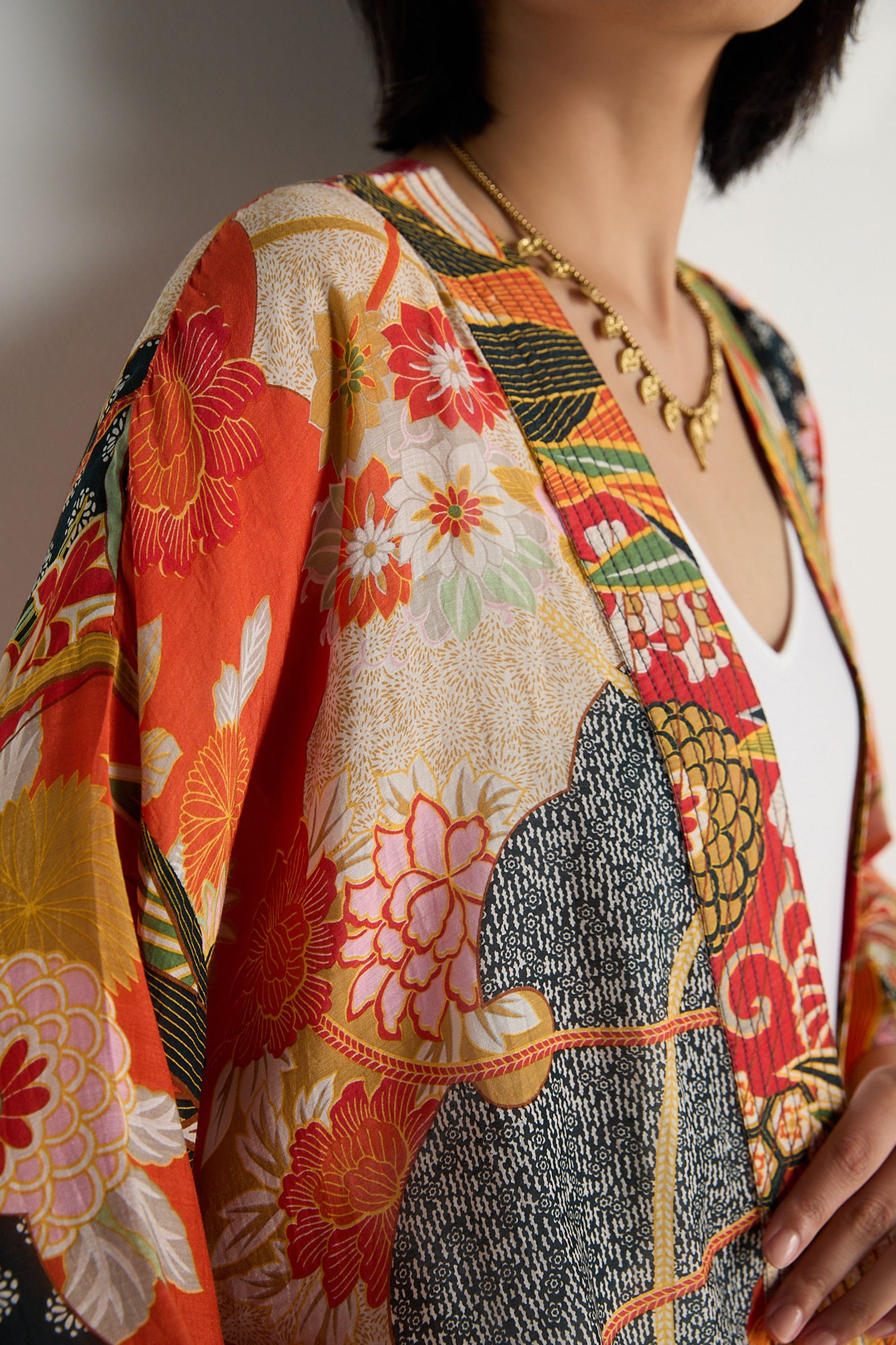 A person wears the Fans Kimono, featuring a bright floral design with subtle fan prints, and a gold necklace, shown from shoulders to mid-torso against a plain background.