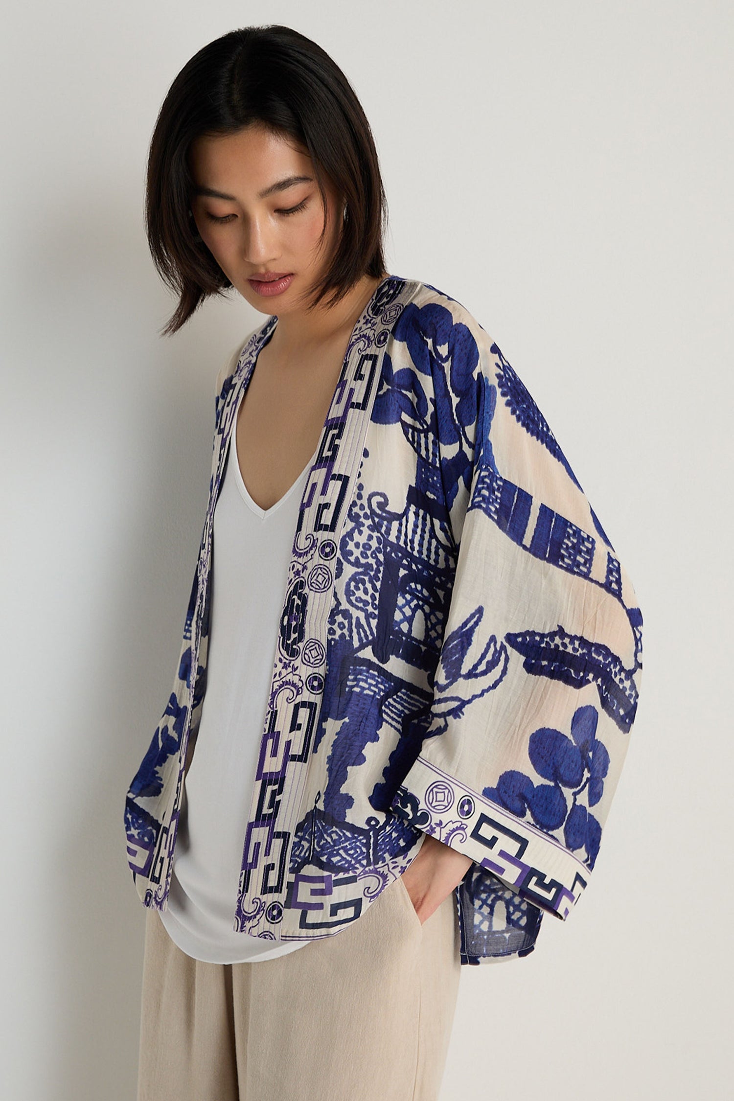 A woman poses against a plain background wearing a white top, beige pants, and the Willow Print Kimono, which features a relaxed silhouette and a blue-and-white motif.