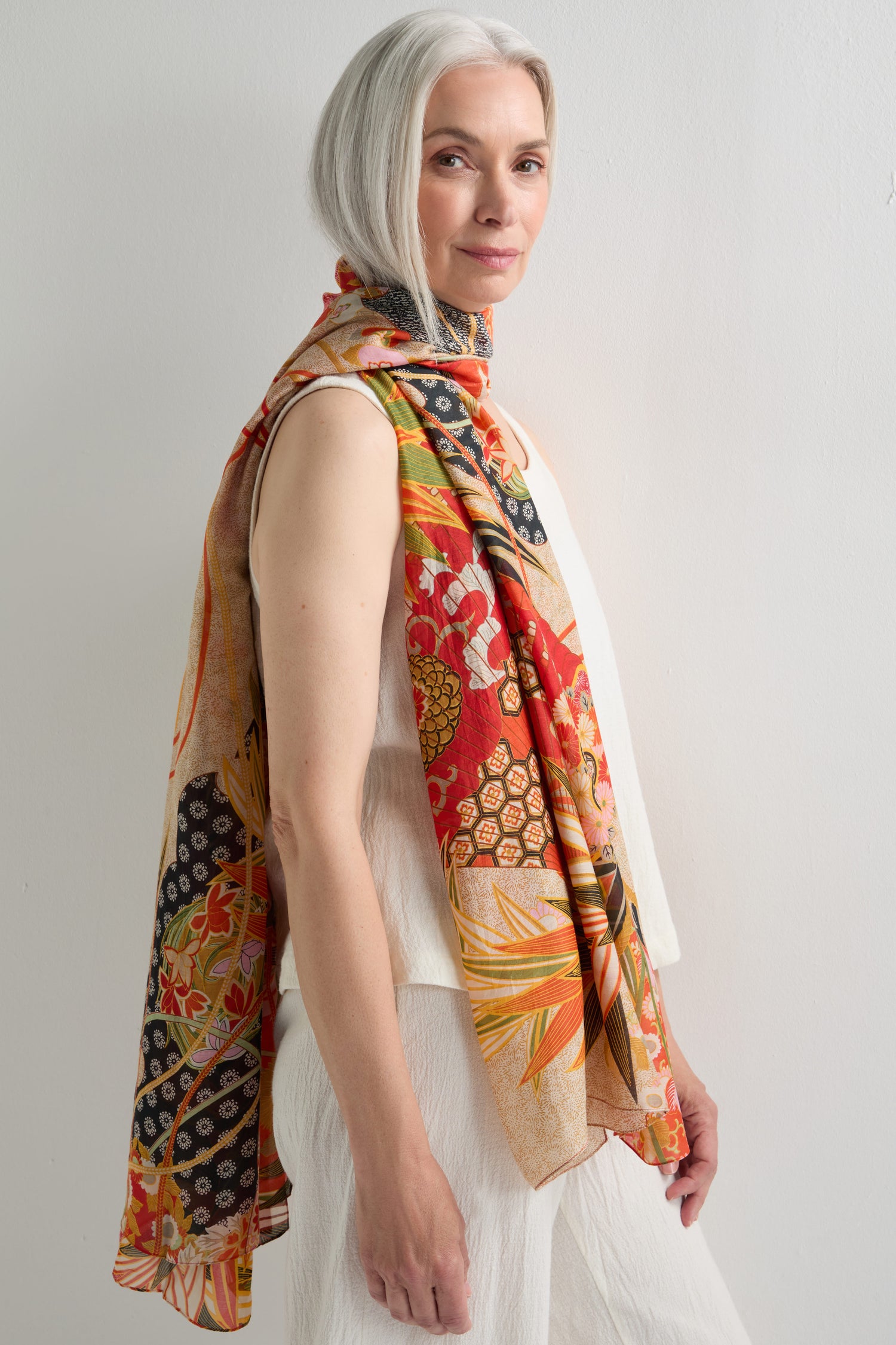 A woman with gray hair stands sideways, wearing a sleeveless white outfit and draping a Fans Print Scarf over her shoulders against a plain light background.