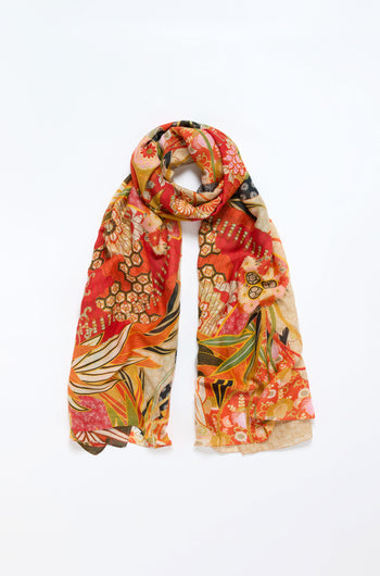 The Fans Print Scarf showcases bold botanical and geometric patterns in red, orange, yellow, and green on a light background, displayed flat with the ends draped down.