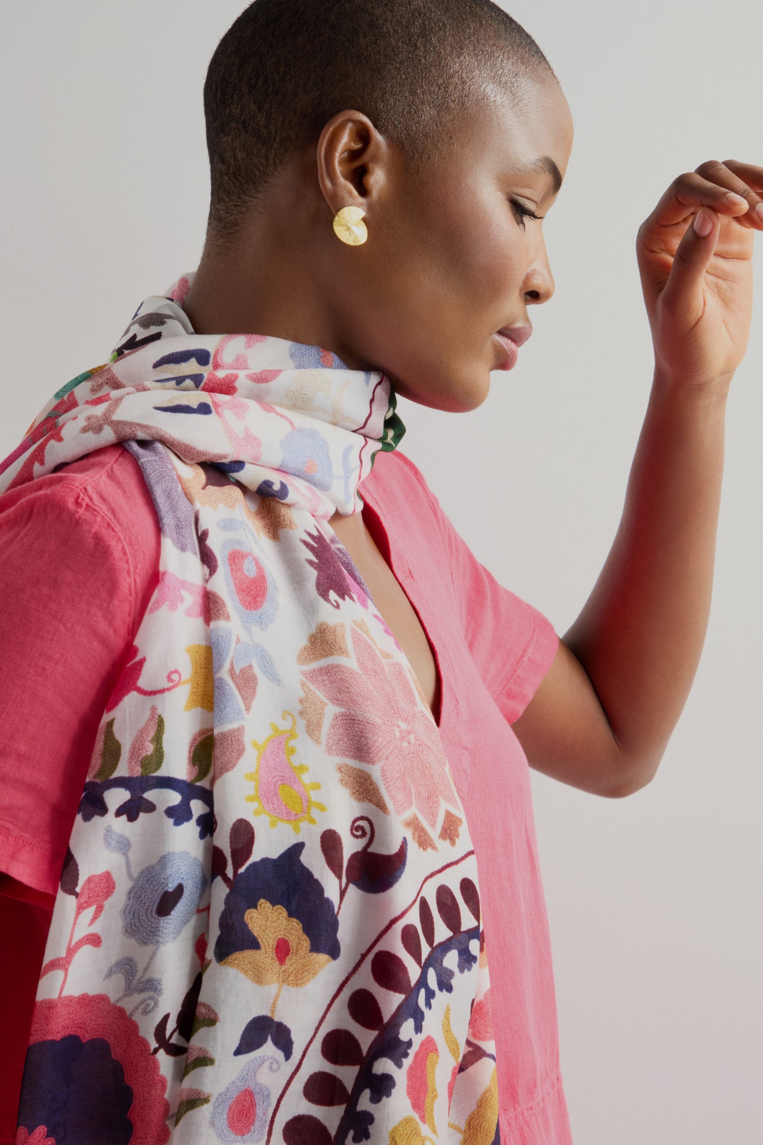 A person in a pink shirt and a Suzani Print Scarf adorned with floral designs looks downwards against a plain background.